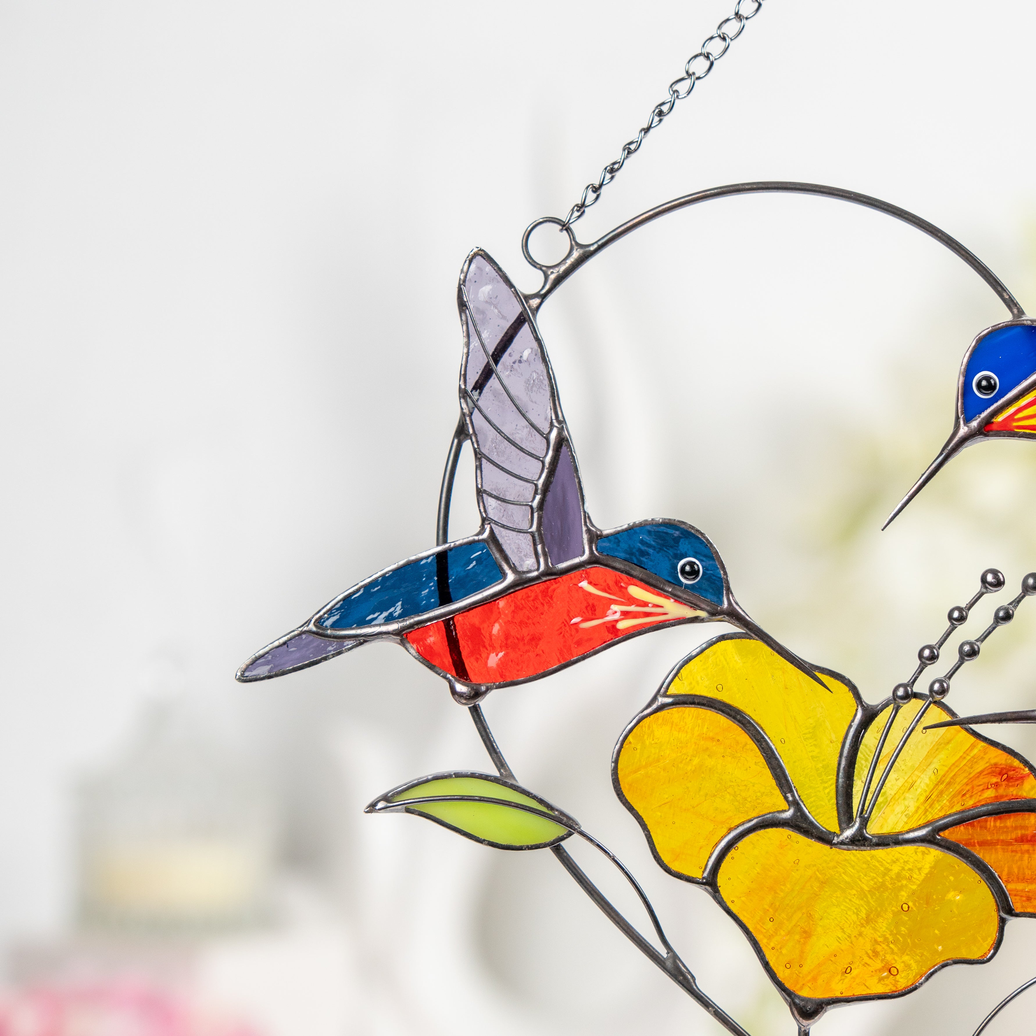 Close-up on yellow and orange stained glass hummingbird with hibiscus.
