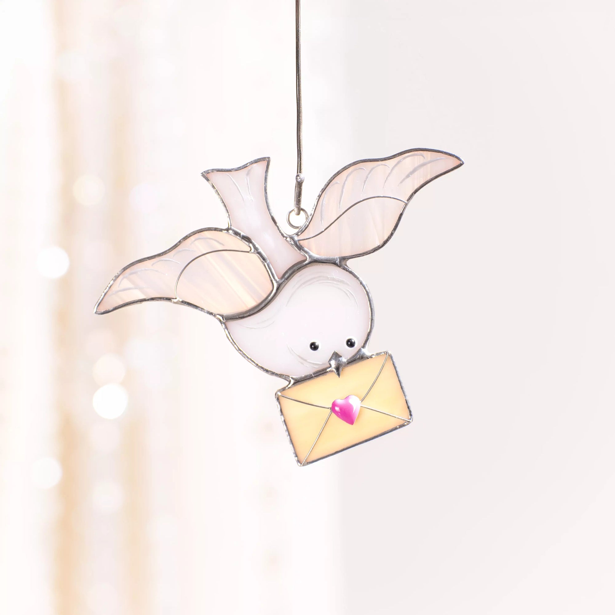 Dove stained glass suncatcher hanging by a ribbon in a softly lit interior.