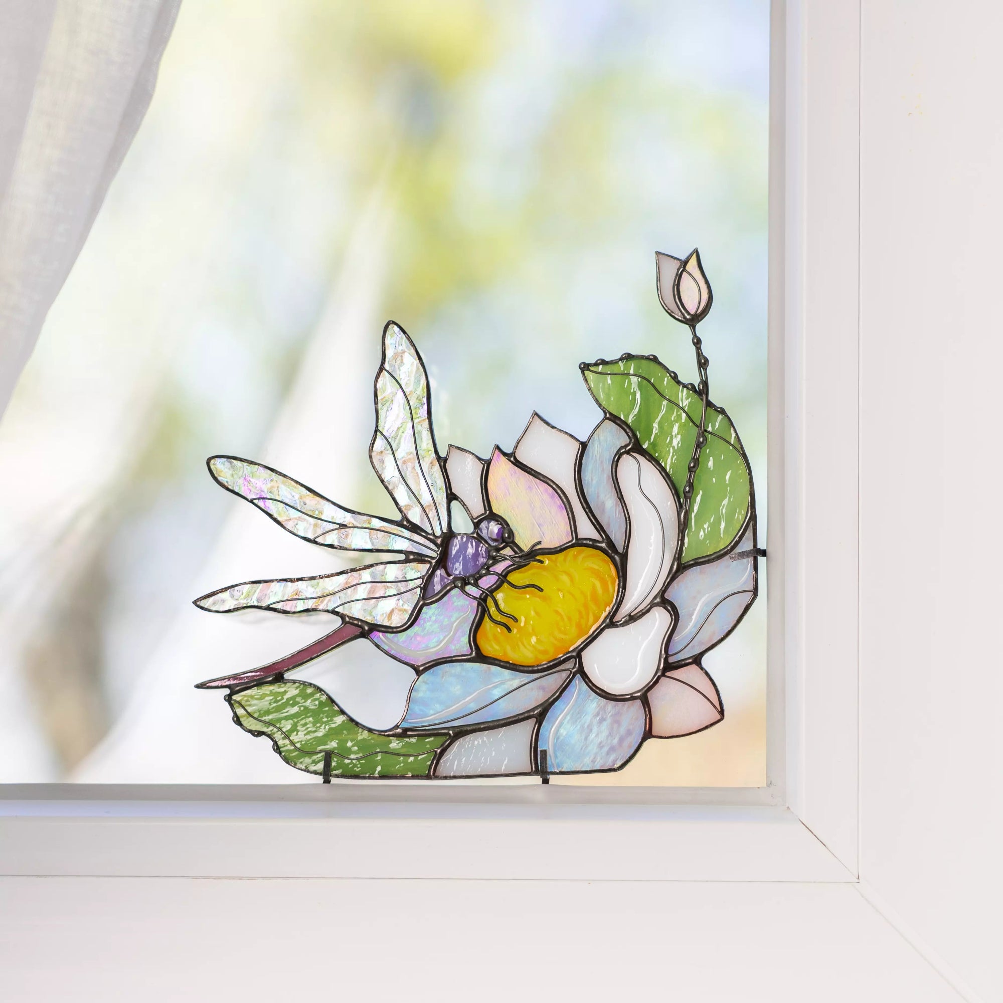 Stained glass dragonfly and flower panel displayed near a window, glowing in natural daylight.