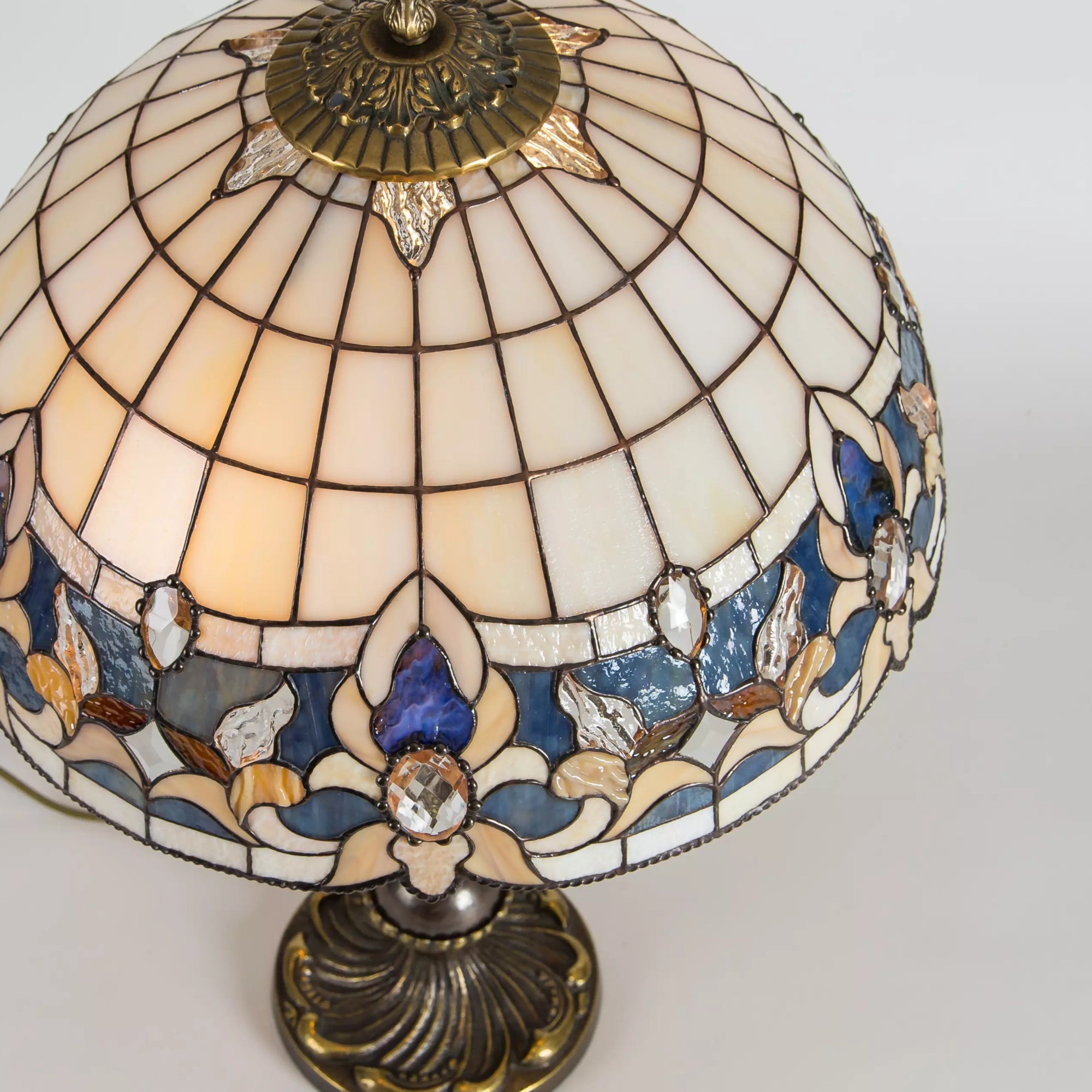 Side view of beige stained glass dome lamp with floral border and ornate bronze base