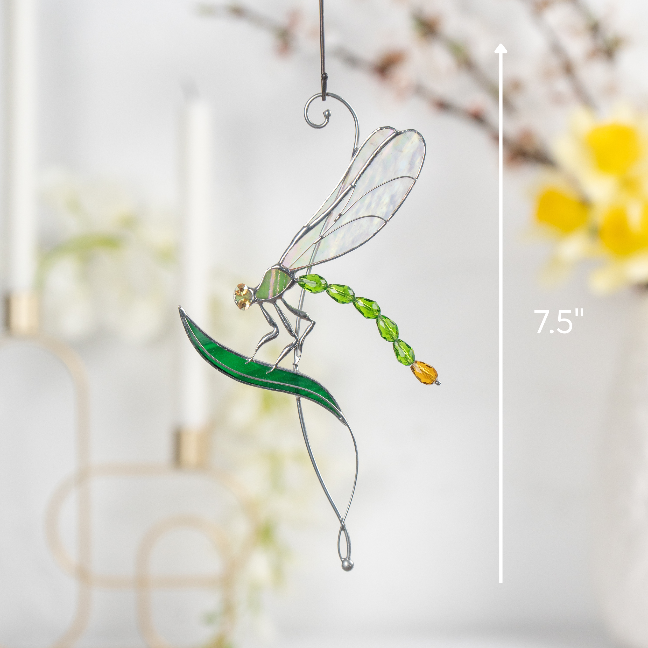 Stained glass dragonfly with labeled 7.5" height hanging in sunlit indoor setting.