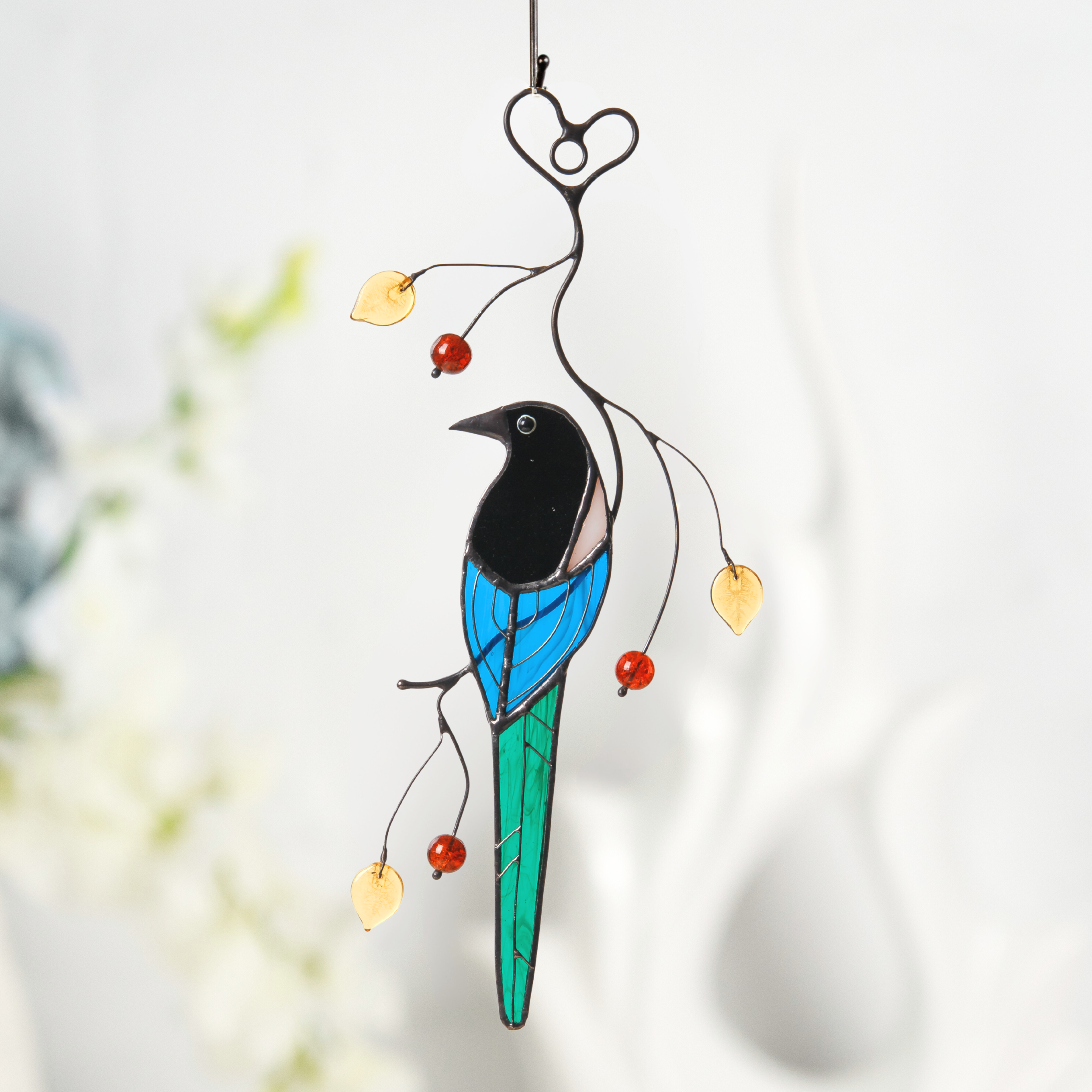Stained glass magpie hanging in a bright room, surrounded by blurred decorative elements.