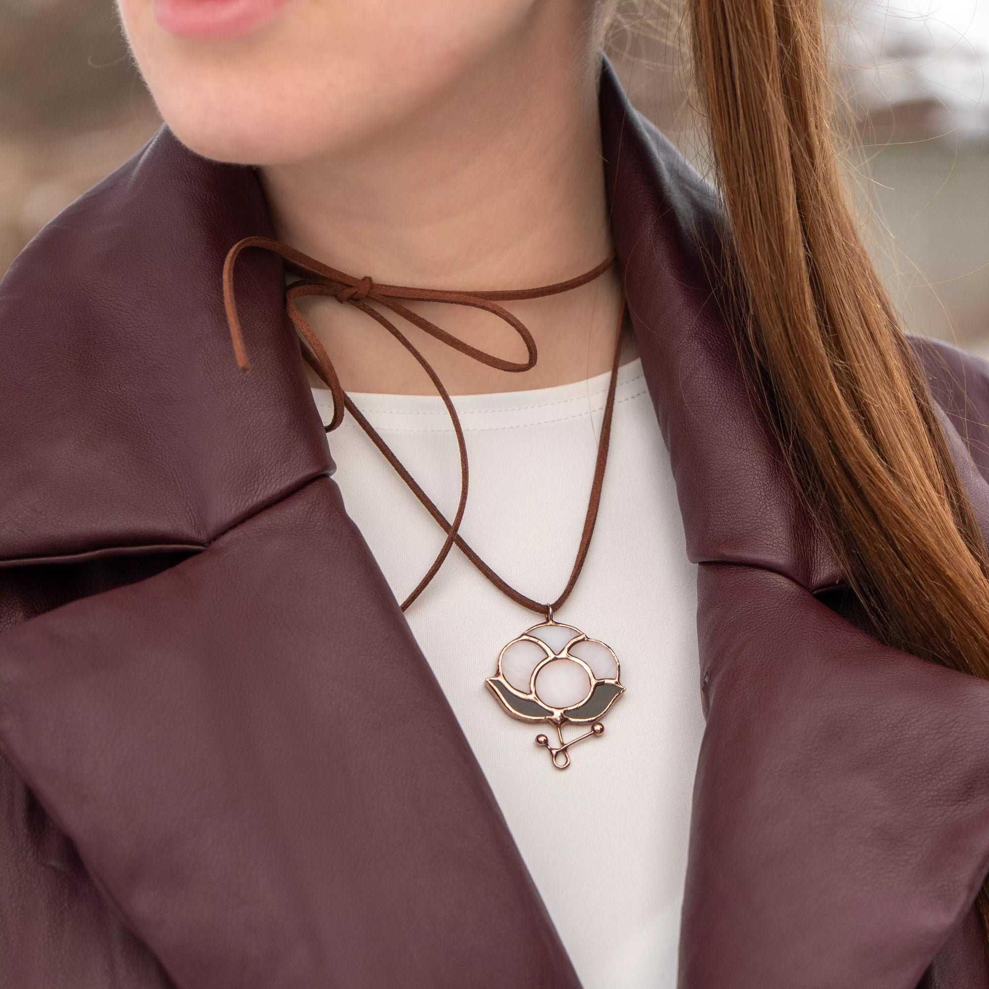 Close-up of woman wearing cotton stained glass pendant tied in bow over a white blouse and maroon jacket
