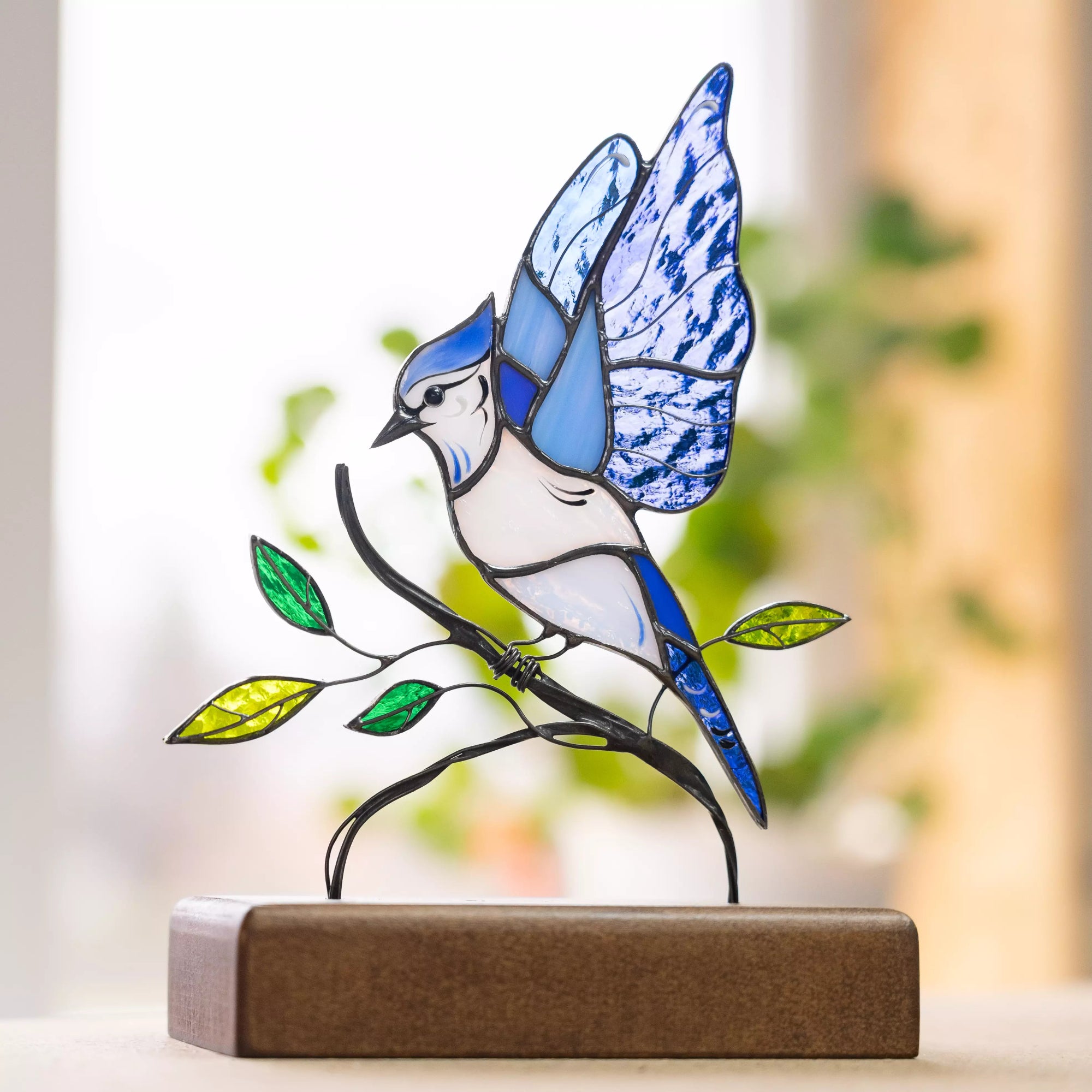 Stained glass bird with patterned wings shown in natural light, greenery in soft background