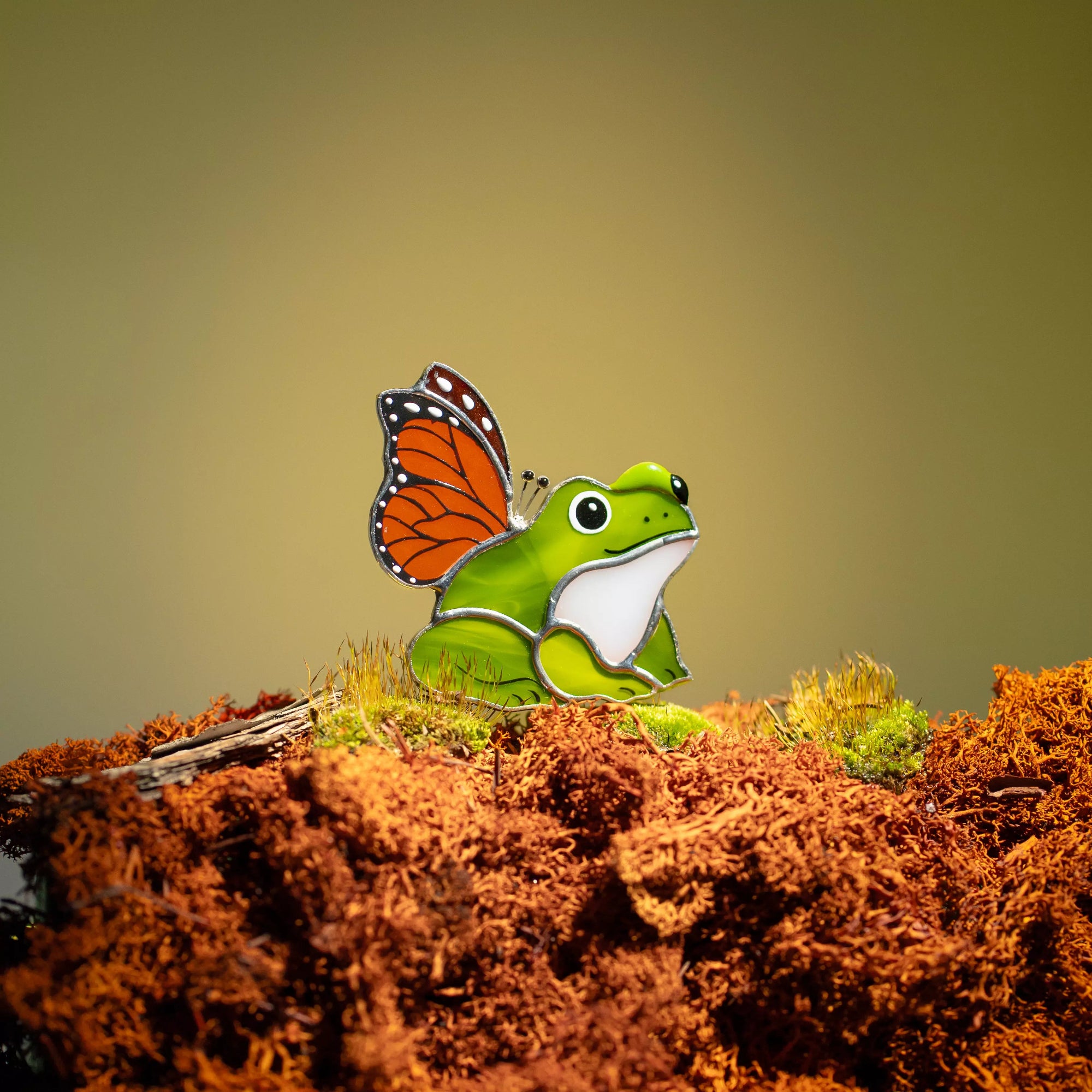 Stained glass frog with butterfly wings on a textured surface