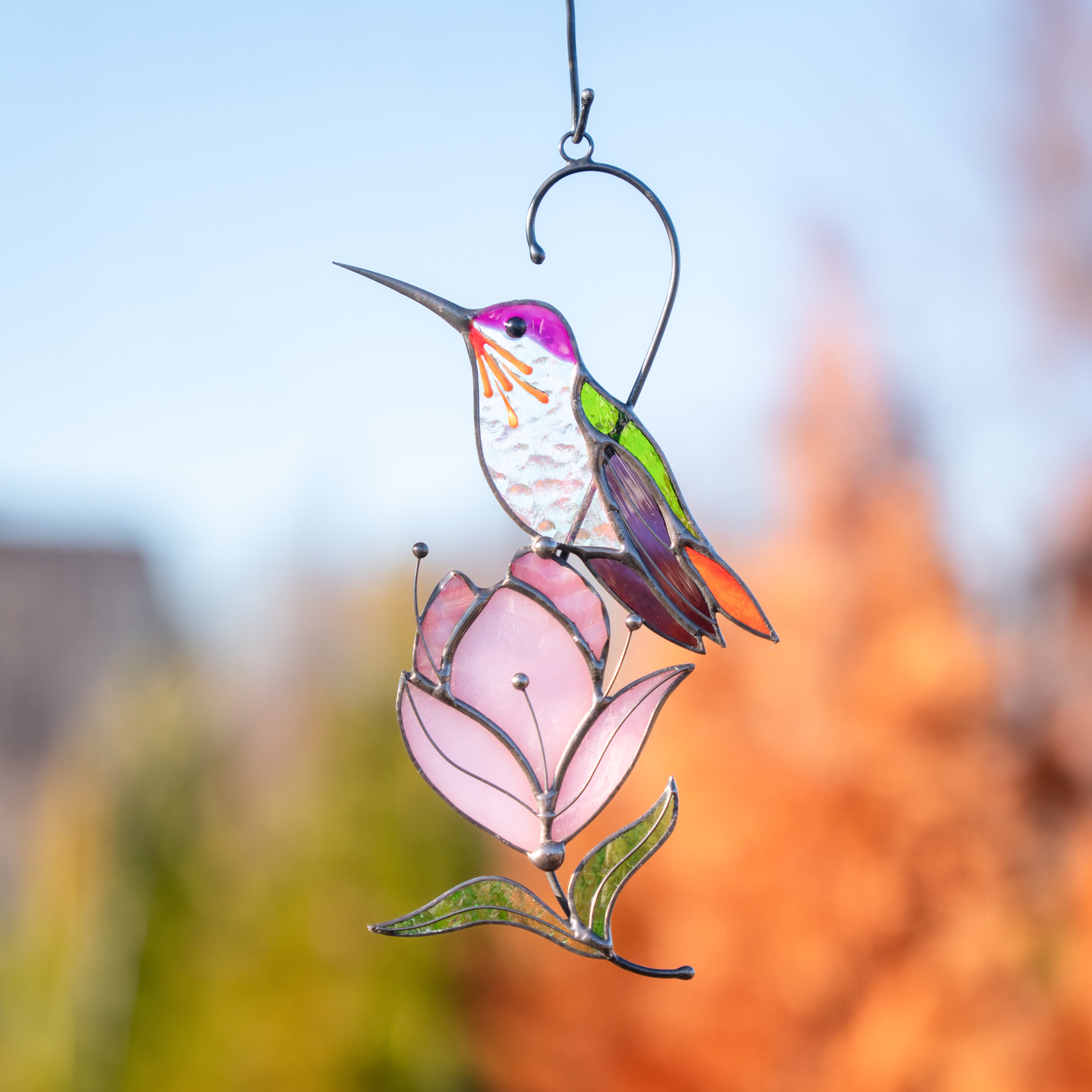 Hummingbird stained glass ornament in vibrant tones perched on magnolia, captured outdoors in golden light.