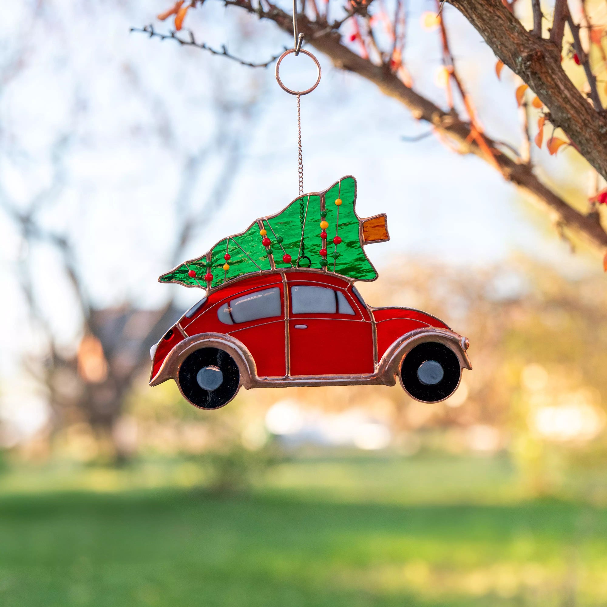 Stained glass suncatcher featuring a red car with a Christmas tree on top, hanging from a tree.