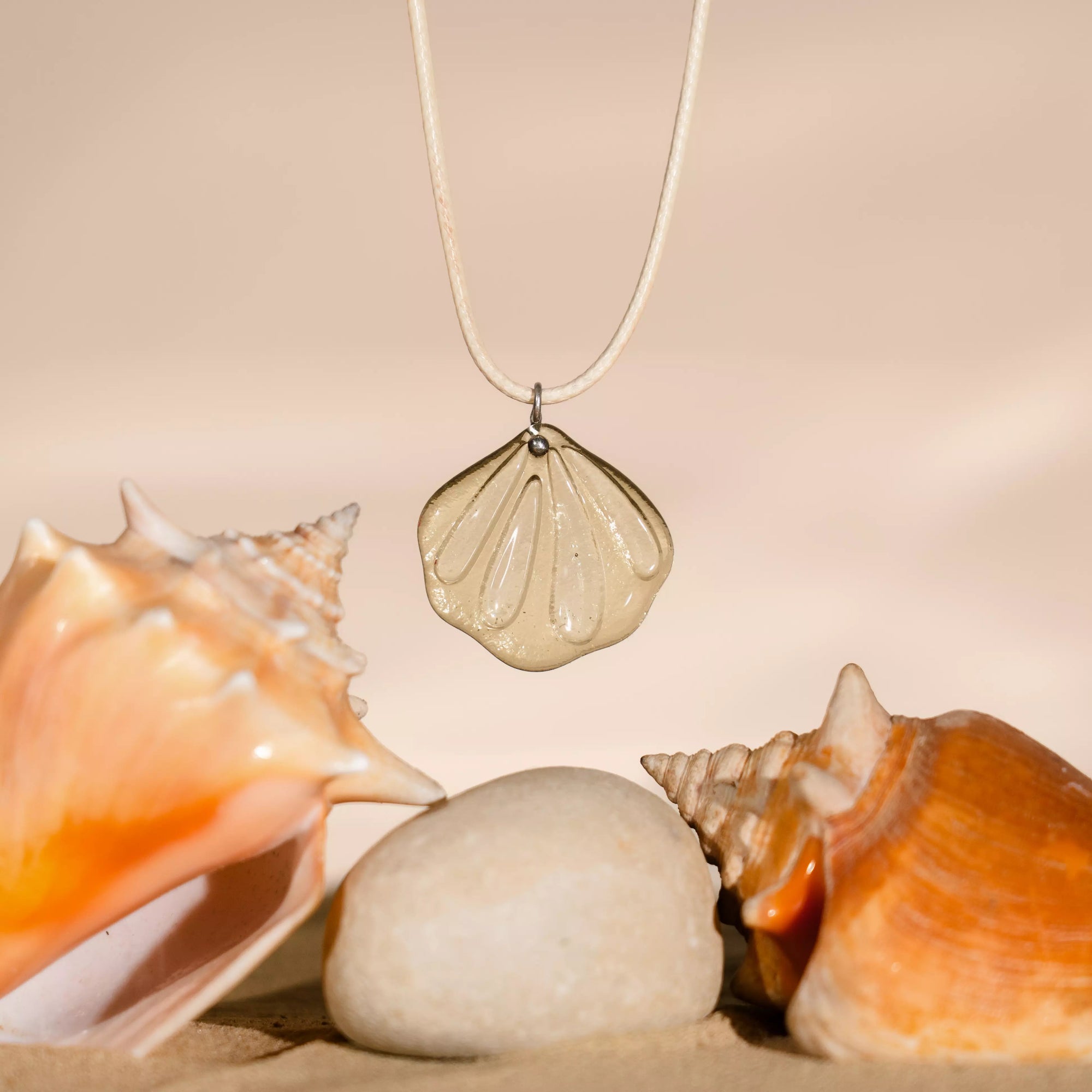 Golden Shell pendant necklace with seashells hanging near real shell fans on a beige background