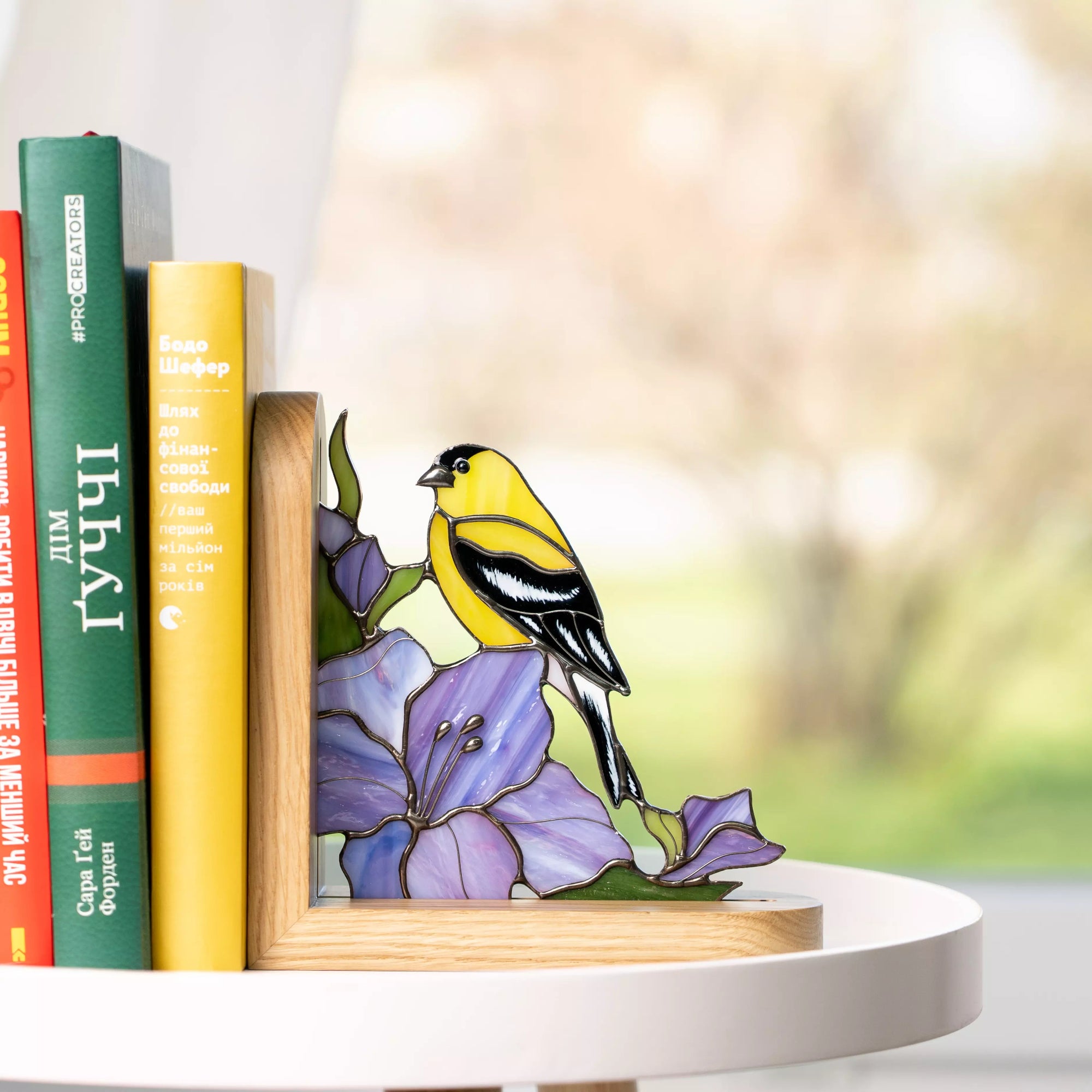 Decorative stained glass bookend with a goldfinch design on a table with books