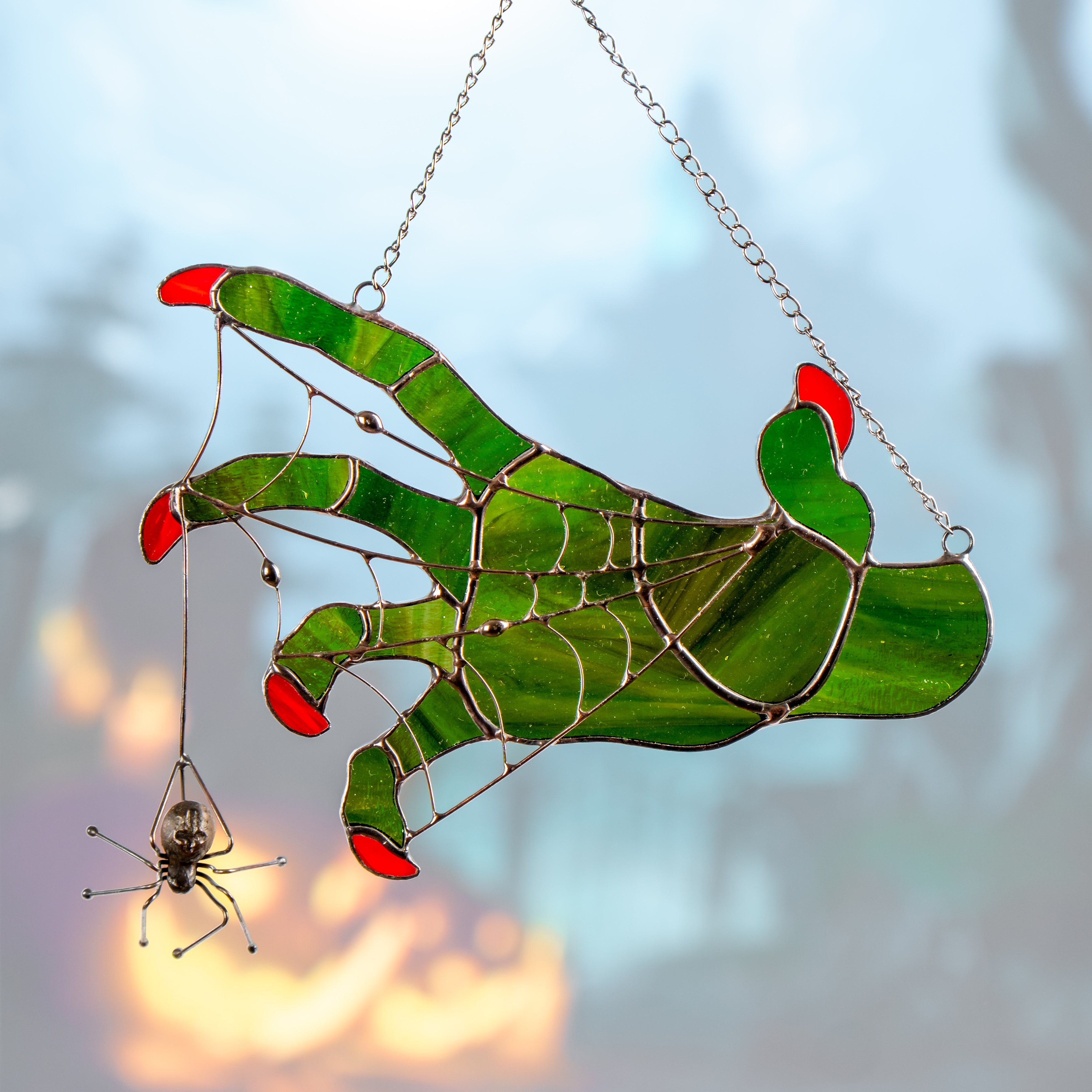 Witch hand with hanging spider shown in glowing light with Halloween-themed background.