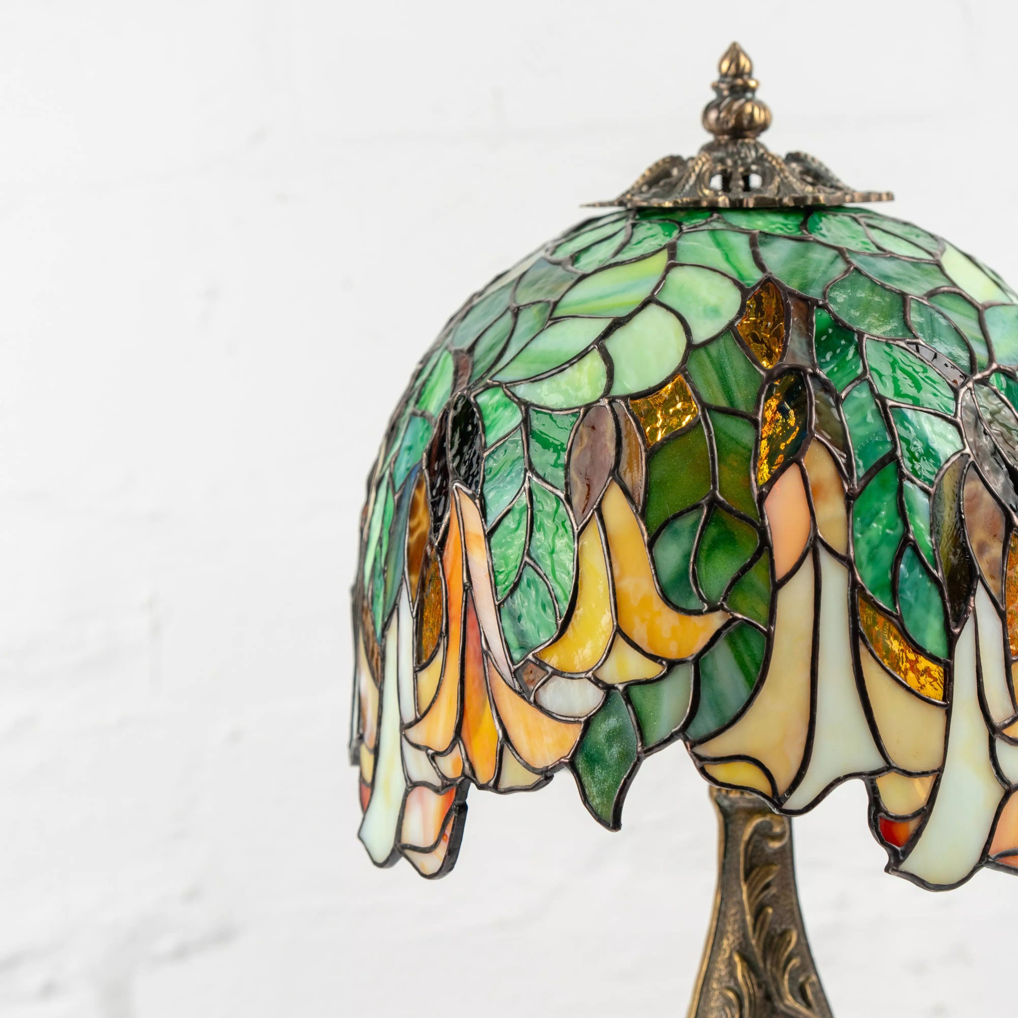Side view of Tiffany style lamp with green leaf and golden flower glass design and antique metal finial on top.