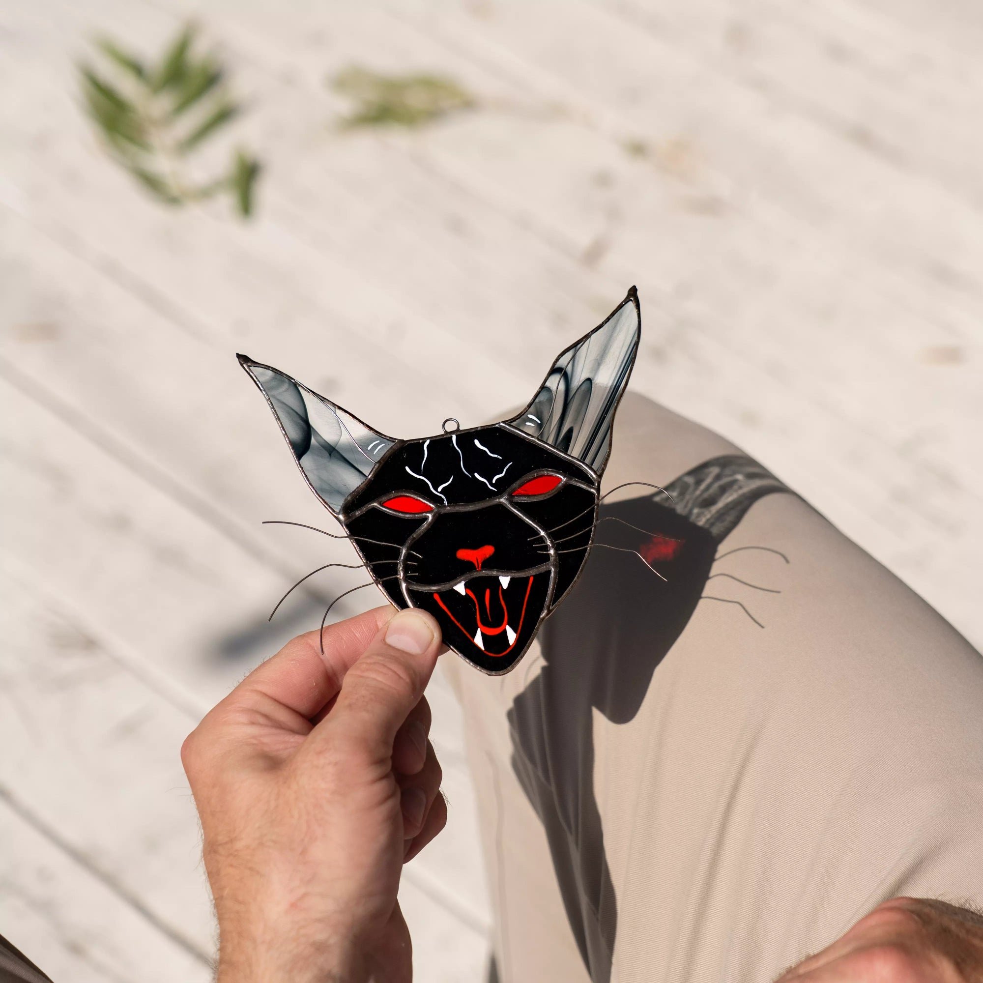 Hand holding a vampire cat suncatcher with red eyes and open mouth against a neutral background