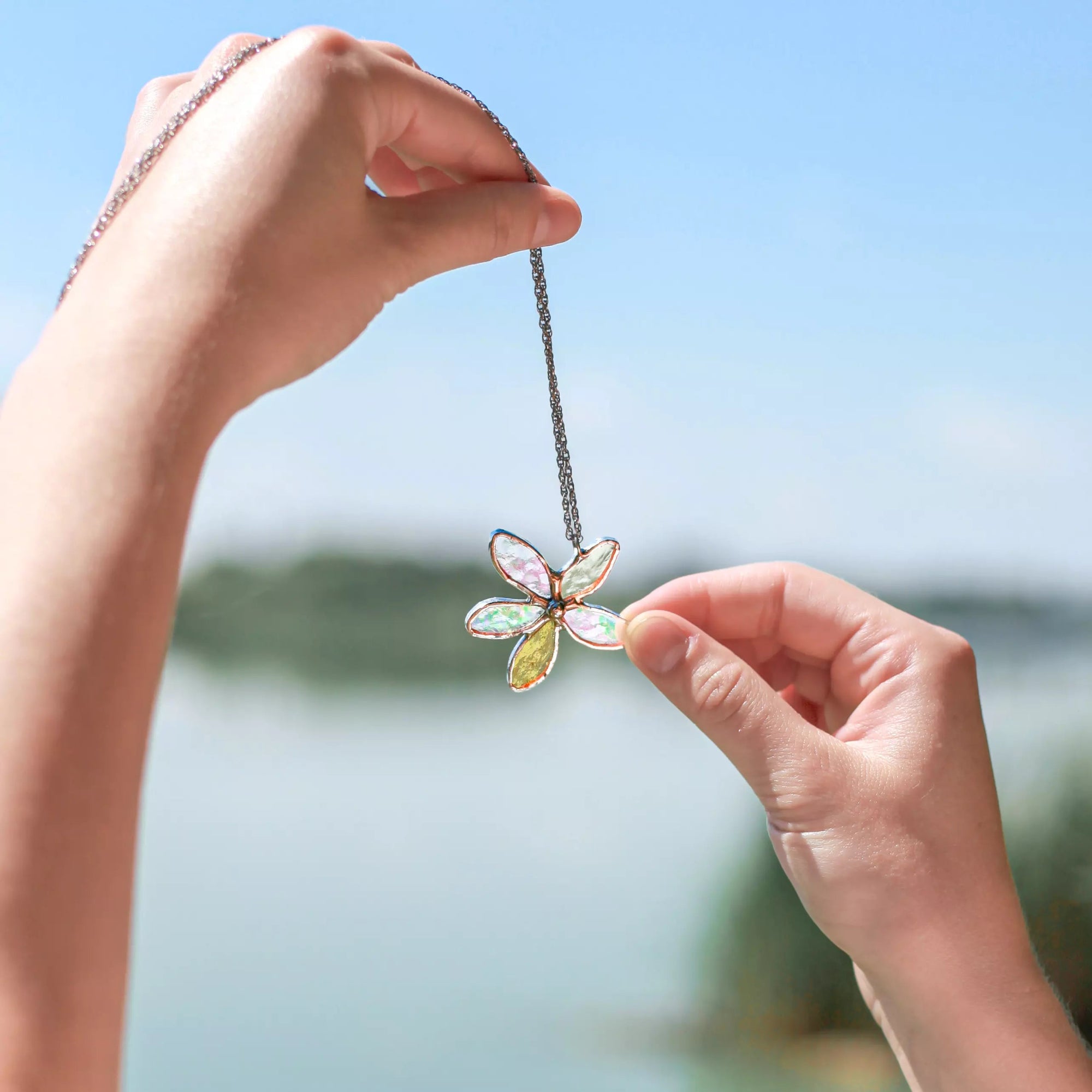 Hand holding a colorful flower-shaped stained glass necklace against a blurred natural background