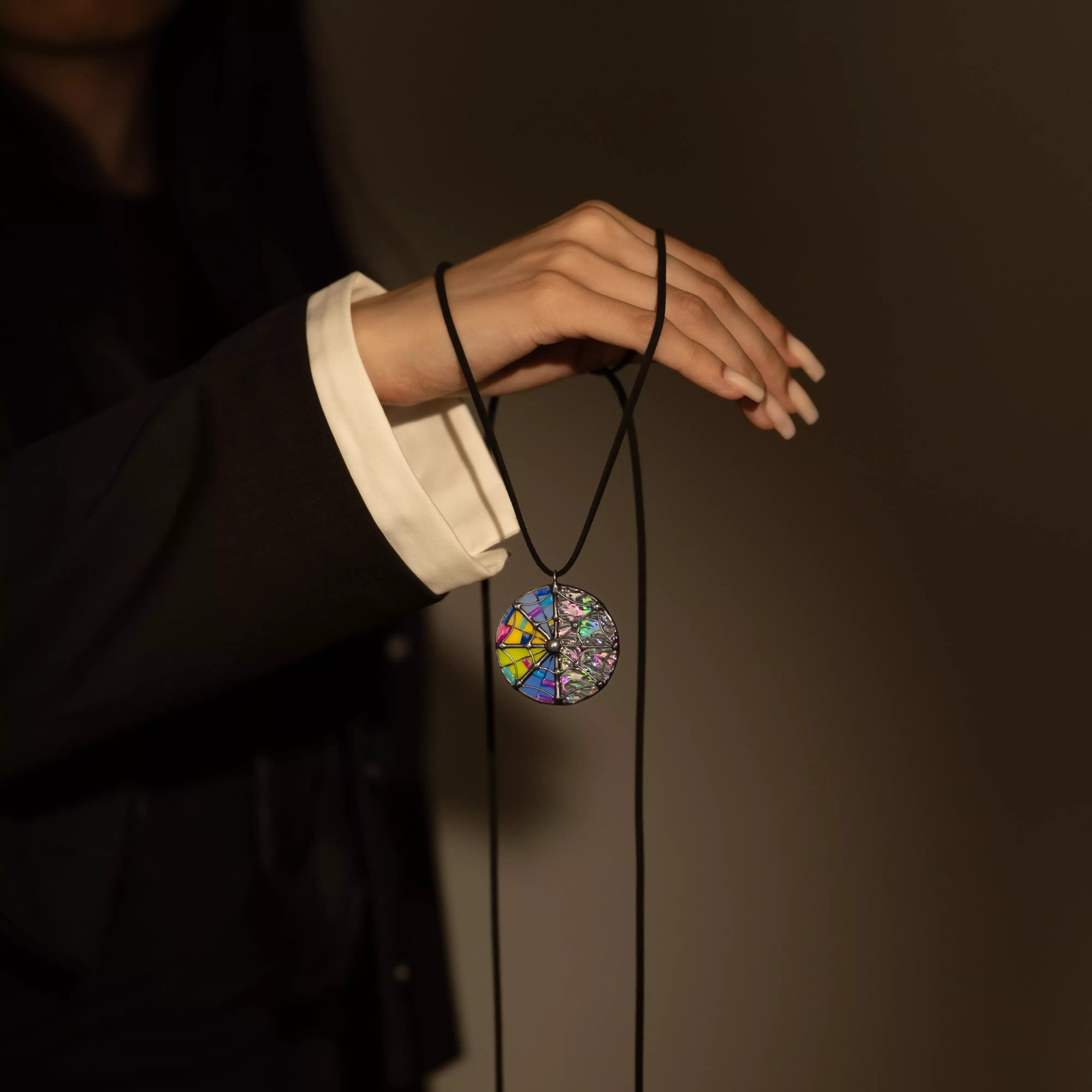 Hand holding a colorful stained glass halloweennpendant necklace against a dark background