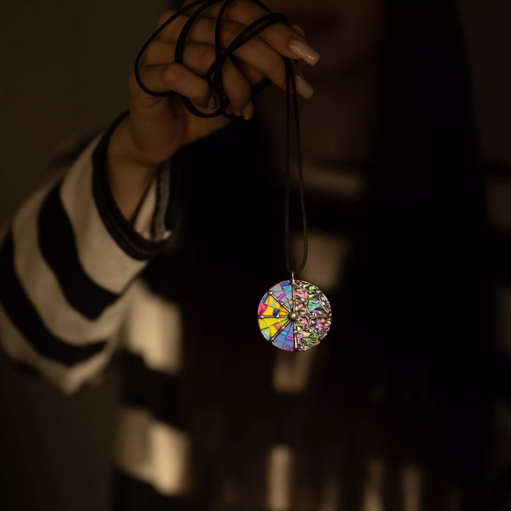 Hand holding a colorful stained glass round pendant with a blurred mystical background