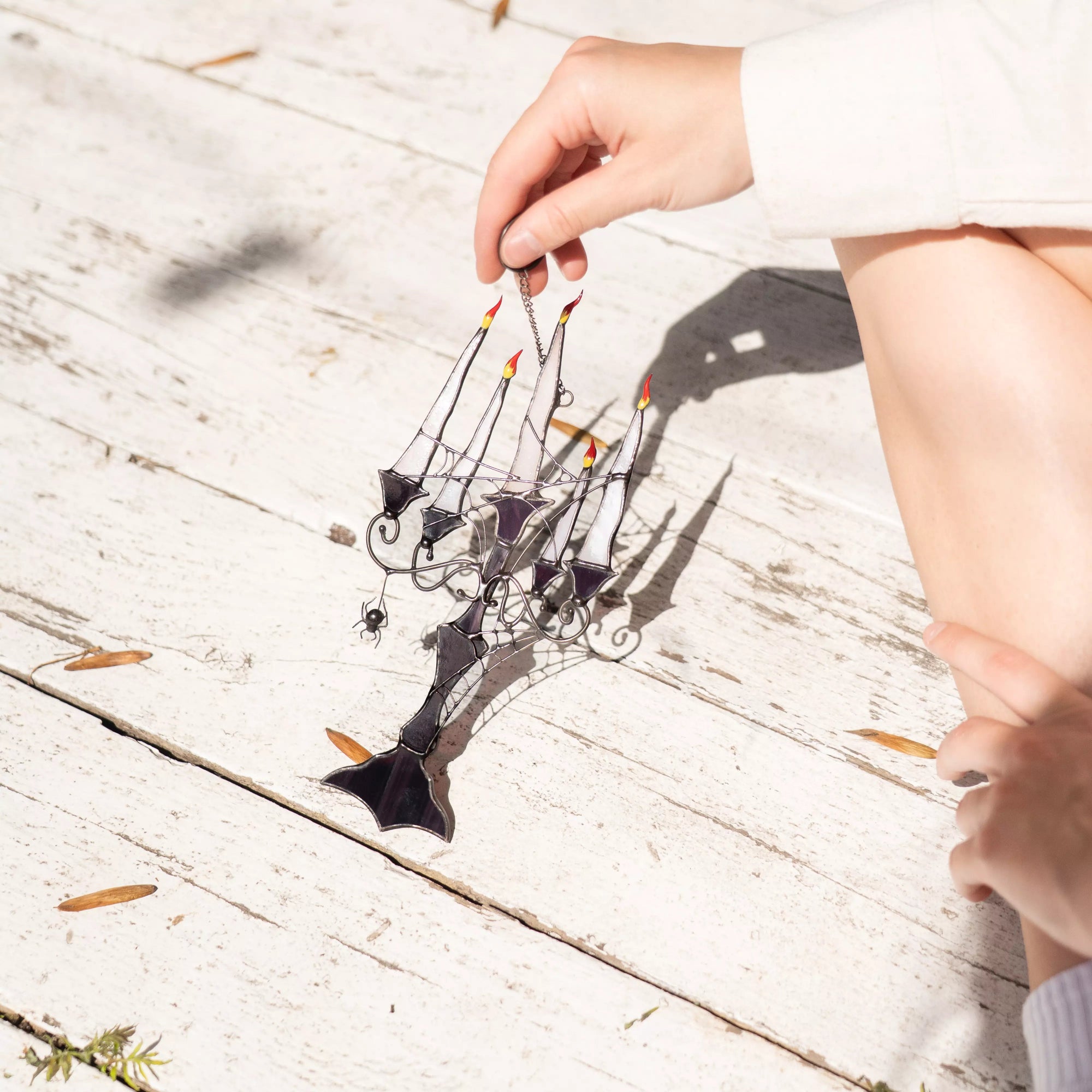 Hand holding a decorative stained glass candelabra suncatcher on a wooden surface