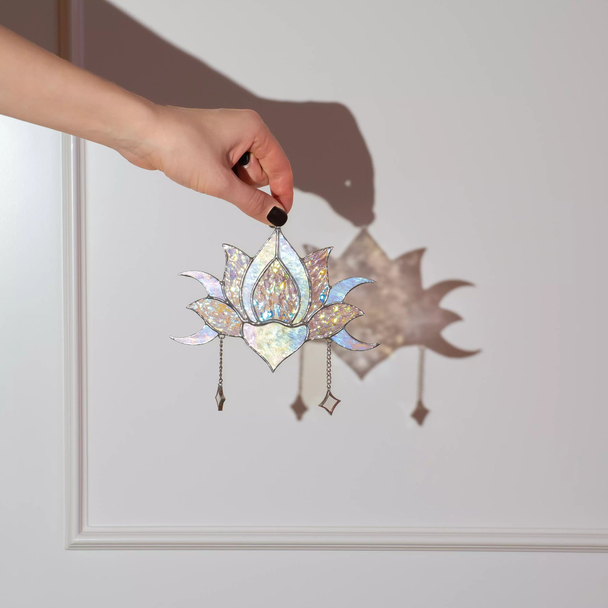 Hand holding a stained glass lotus flower ornament against a plain background