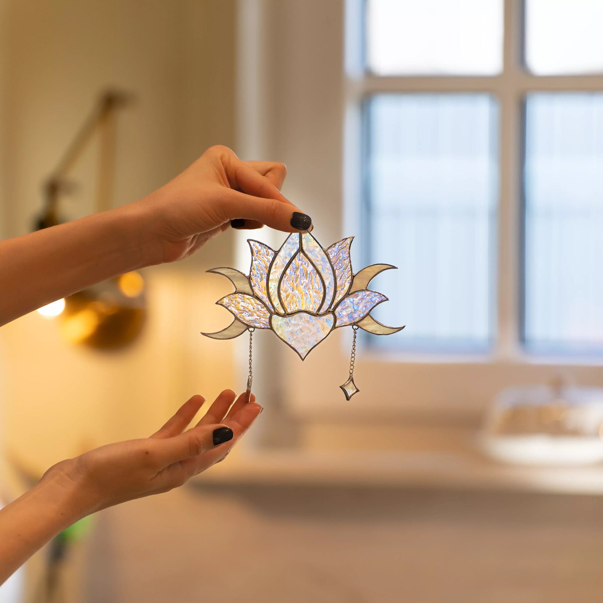 Hand holding stained glass lotus flower suncatcher in a softly blurred indoor setting.