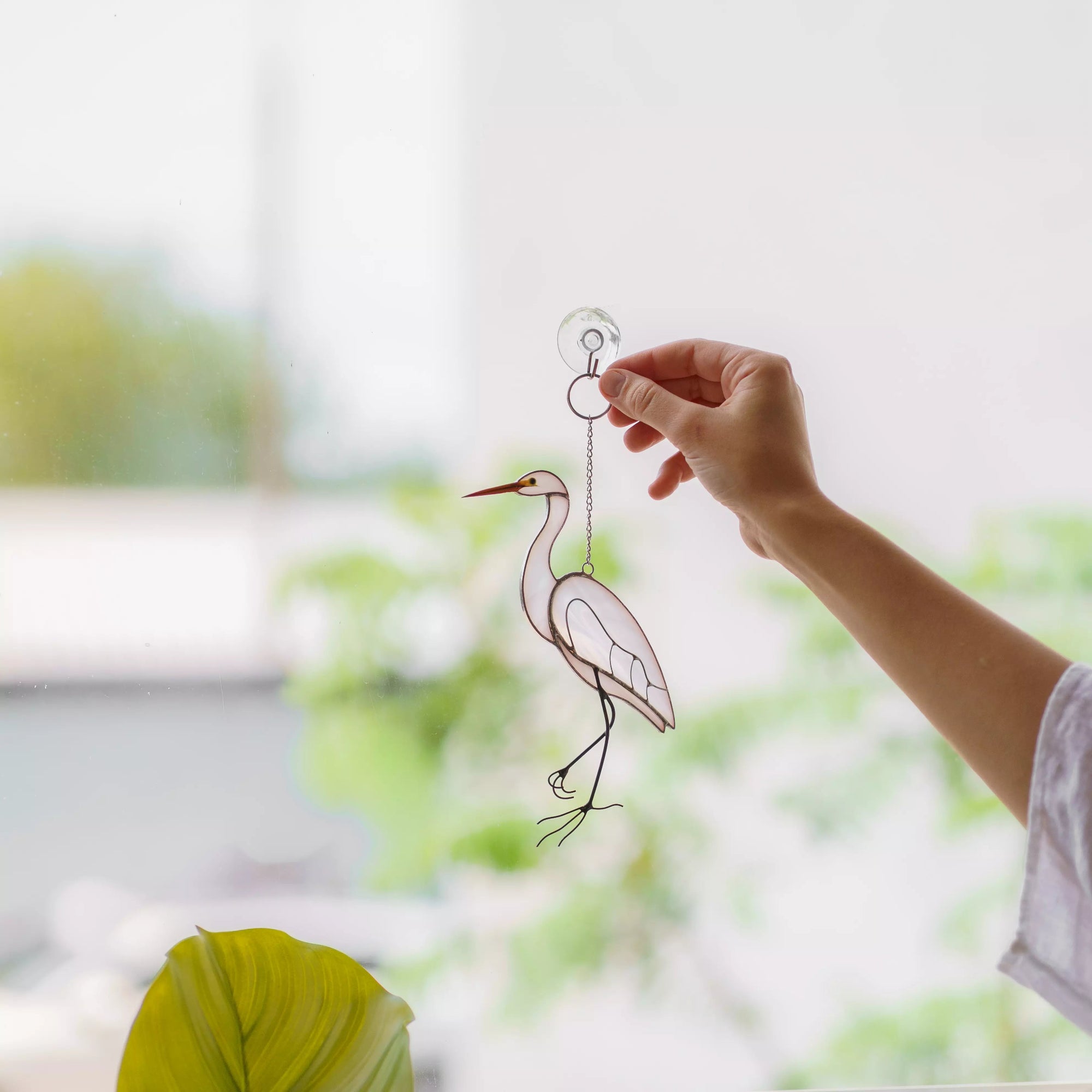 Hand holding stained glass heron suncatcher with a blurred natural background