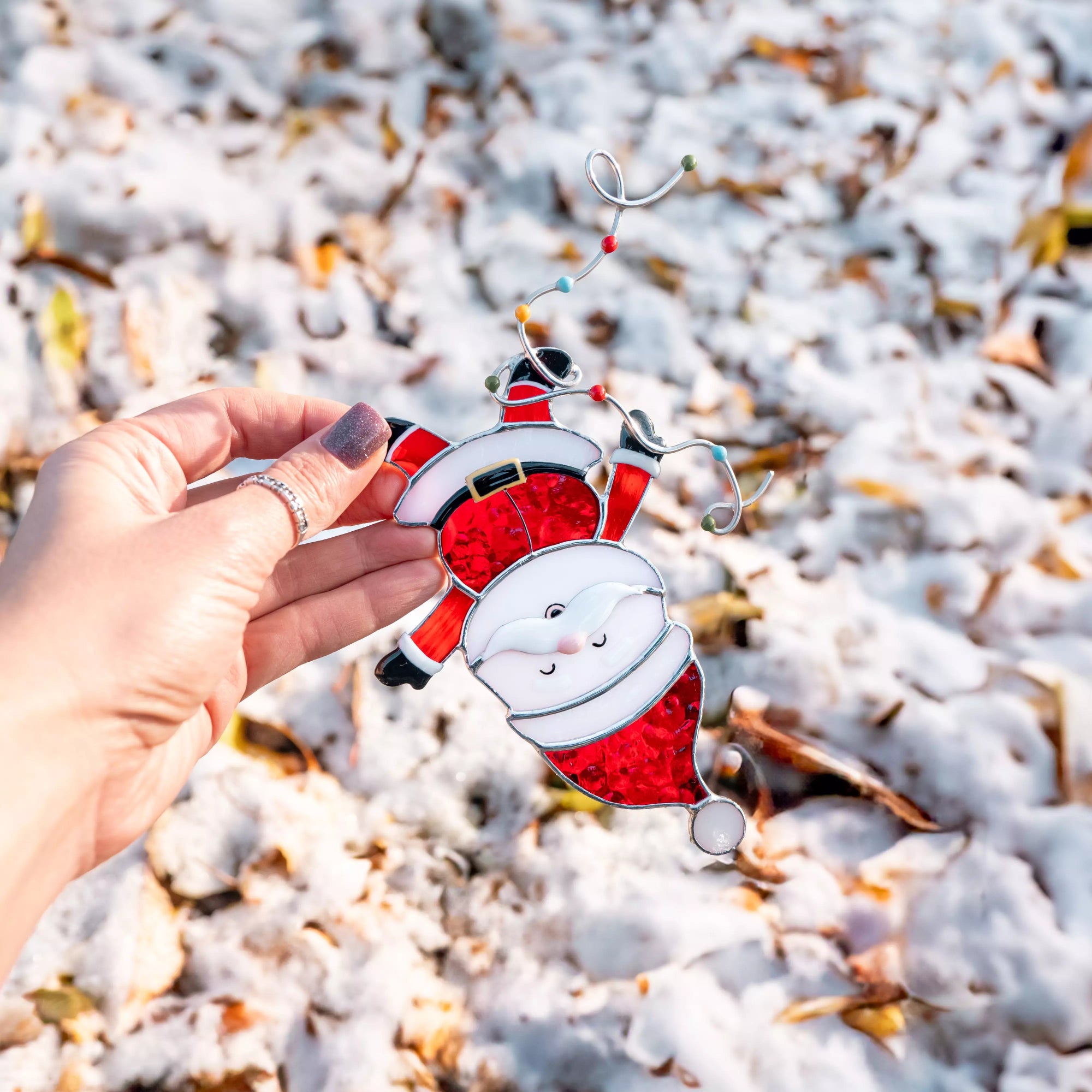 Hand holding a red and white Santa Claus ornament against a snowy background
