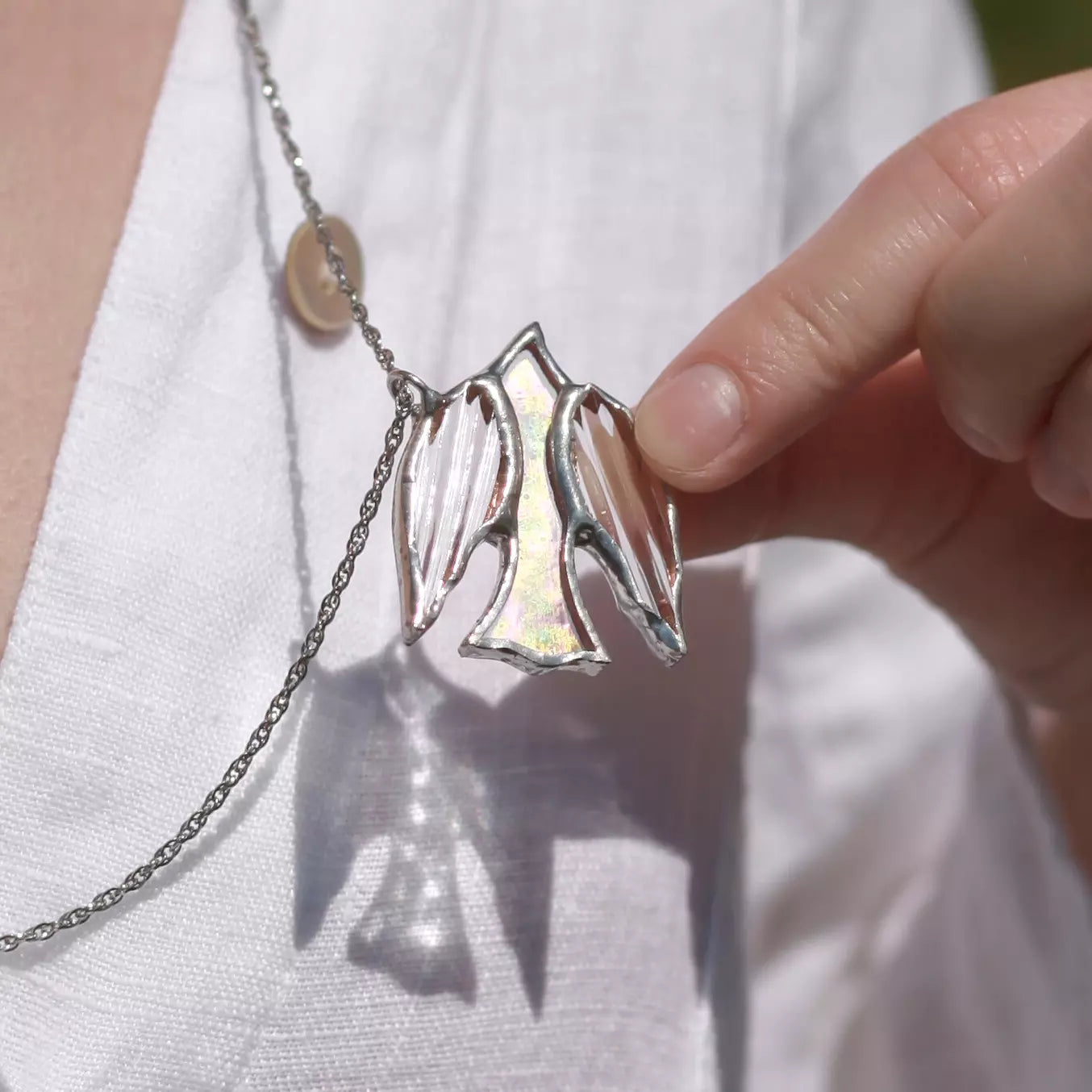 Hand holding a stained glass necklace with a unique pendant against a white background