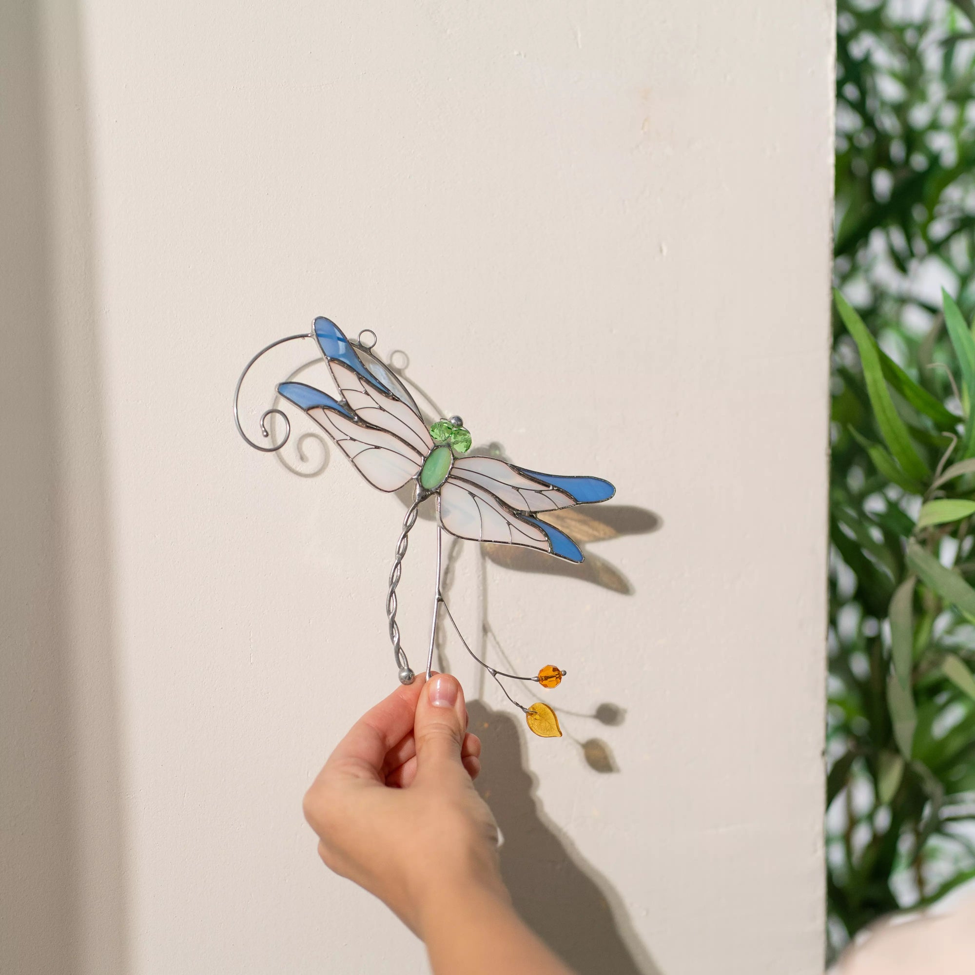 Stained glass dragonfly casting shadow against a neutral wall