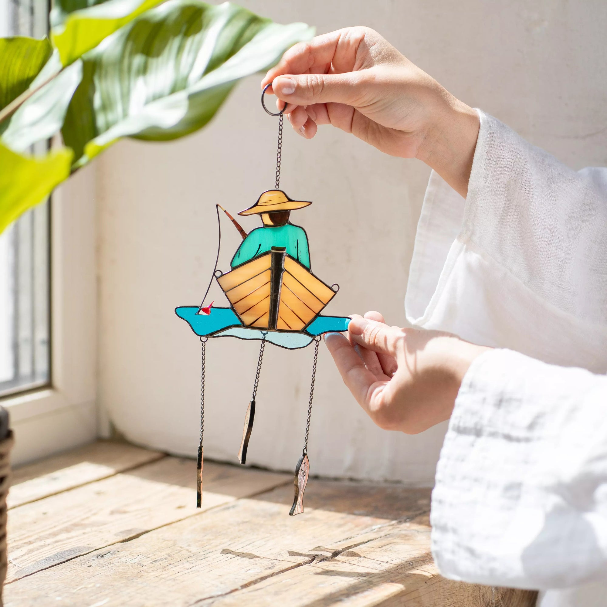 Hand holding a stained glass fisherman suncather with a white background