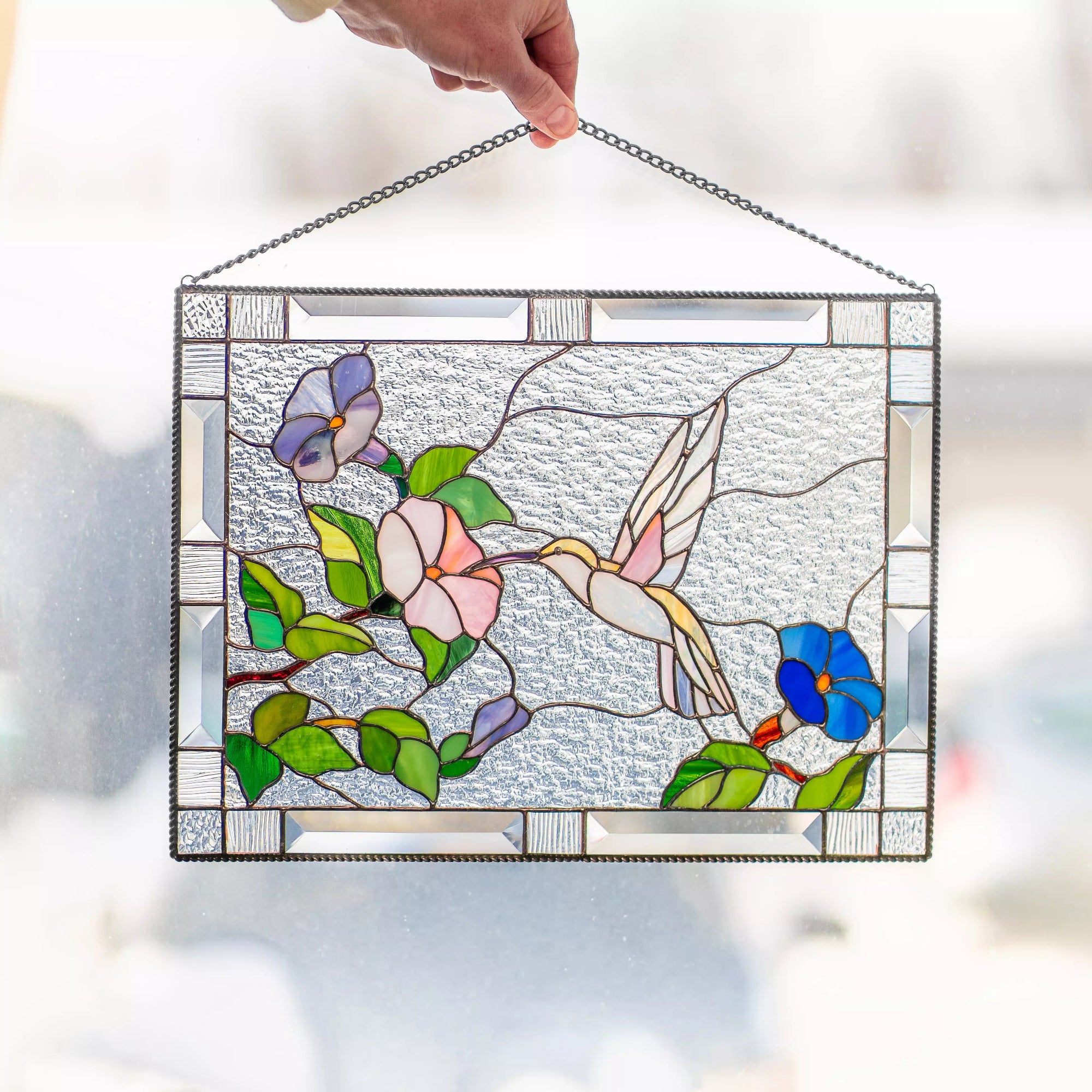 Hand holding stained glass panel featuring a hummingbird and flowers