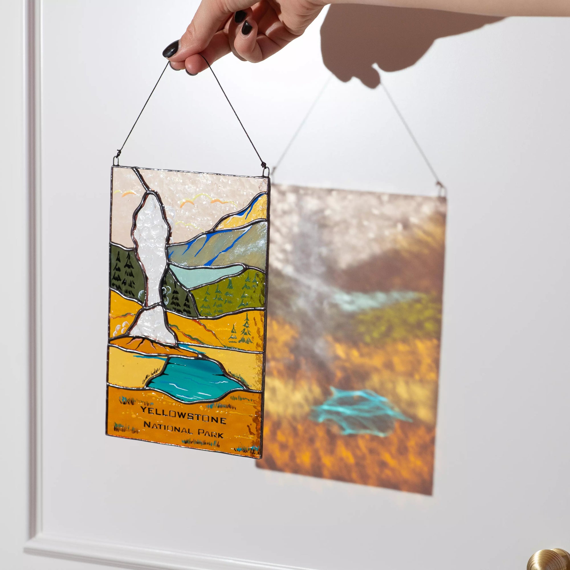 A Yellowstone geyser stained glass panel casting a warm amber and blue shadow on a white wall.