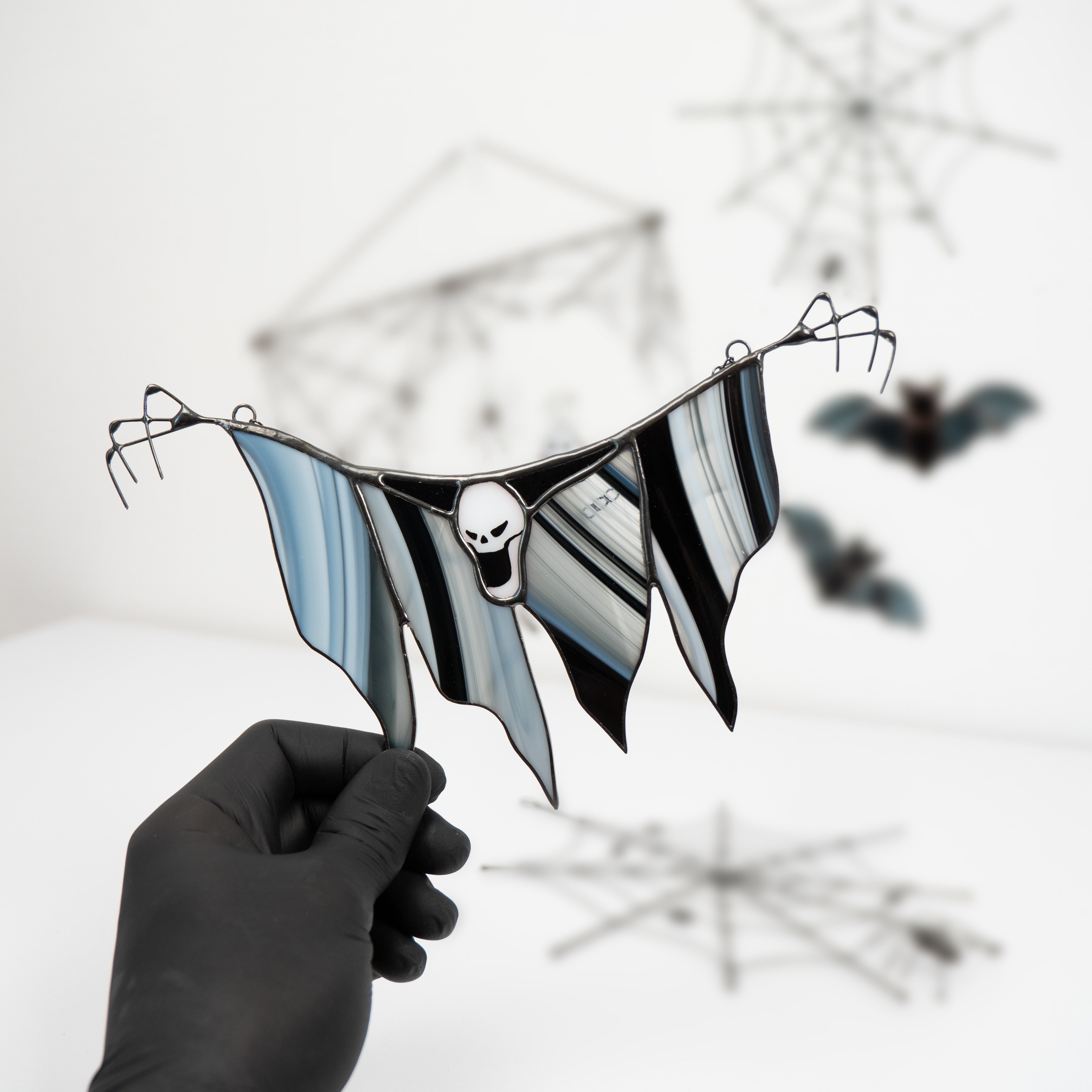 Person holding stained glass Grim Reaper suncatcher with Halloween-decorated background.