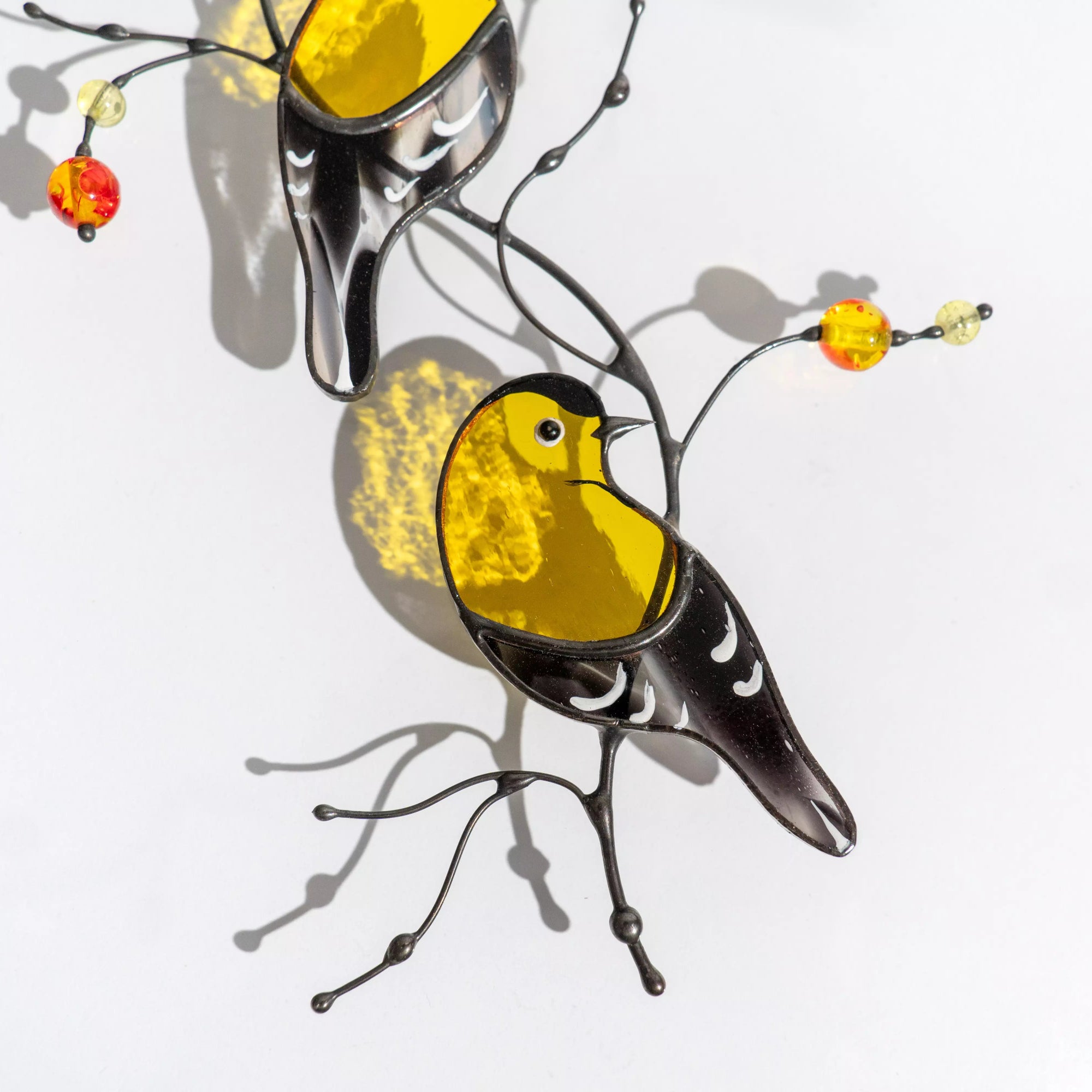 A close-up of the handcrafted bird suncatcher featuring textured yellow glass and delicate white wing details, illuminated by warm light.