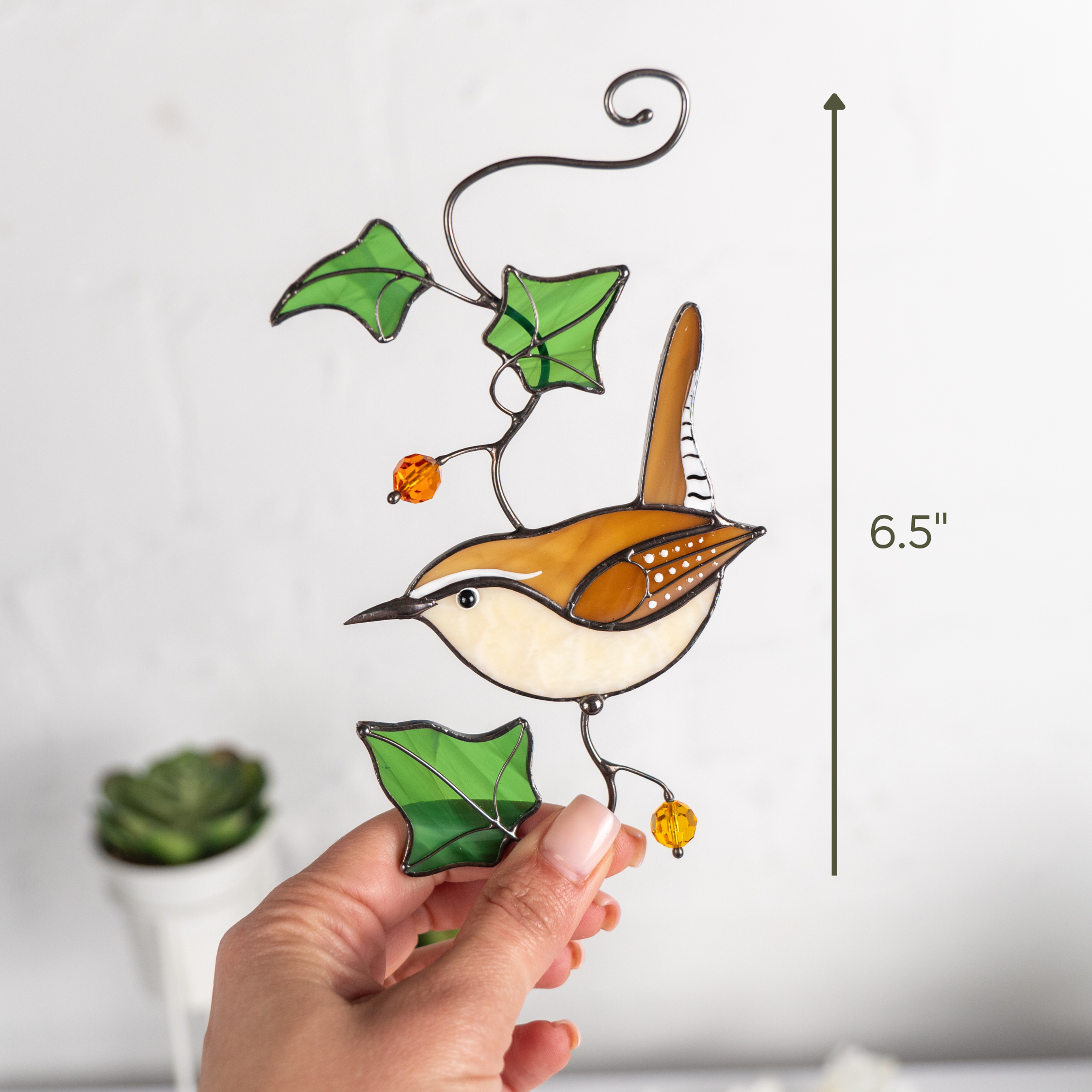 Person holding a Carolina wren suncatcher to show its size as 6.5 inches, with decorative ivy leaves and bright beads.