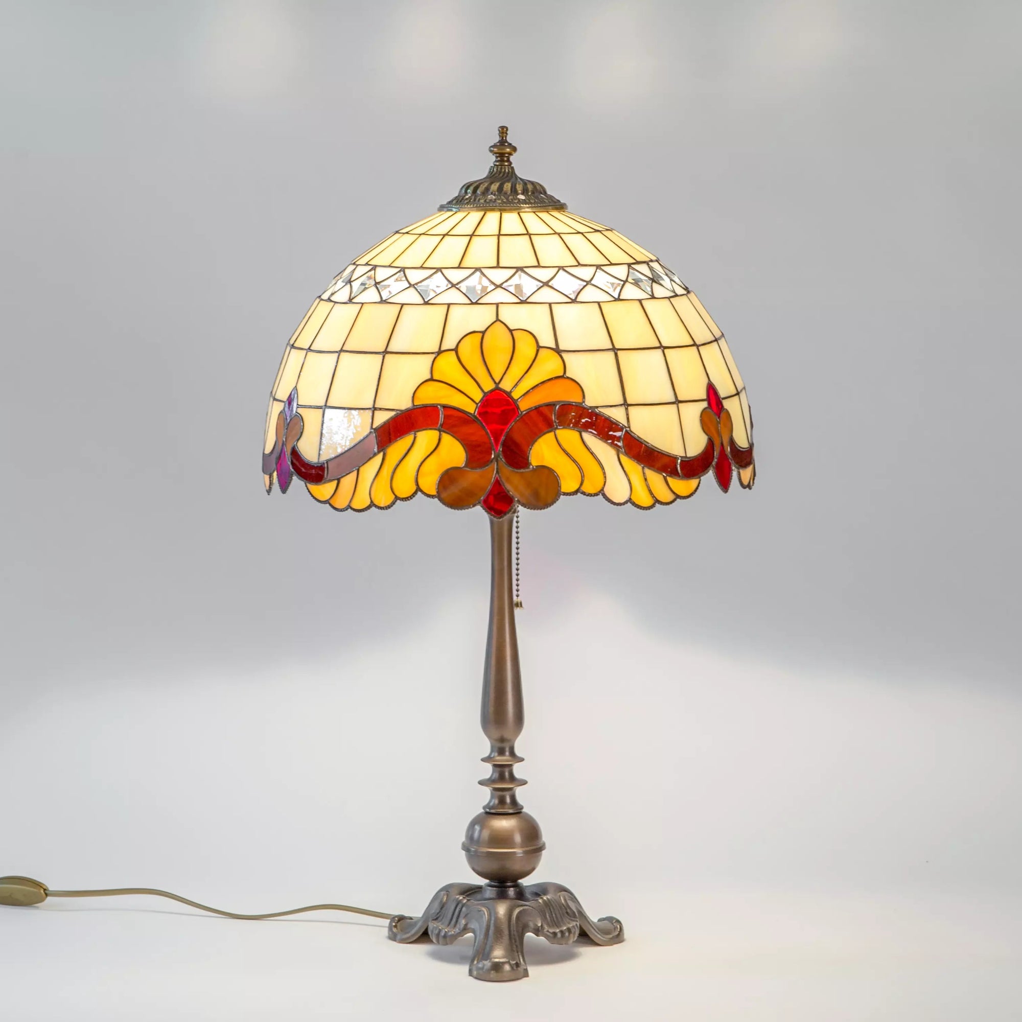 Lit stained glass lamp on metal base with floral amber and red pattern glowing