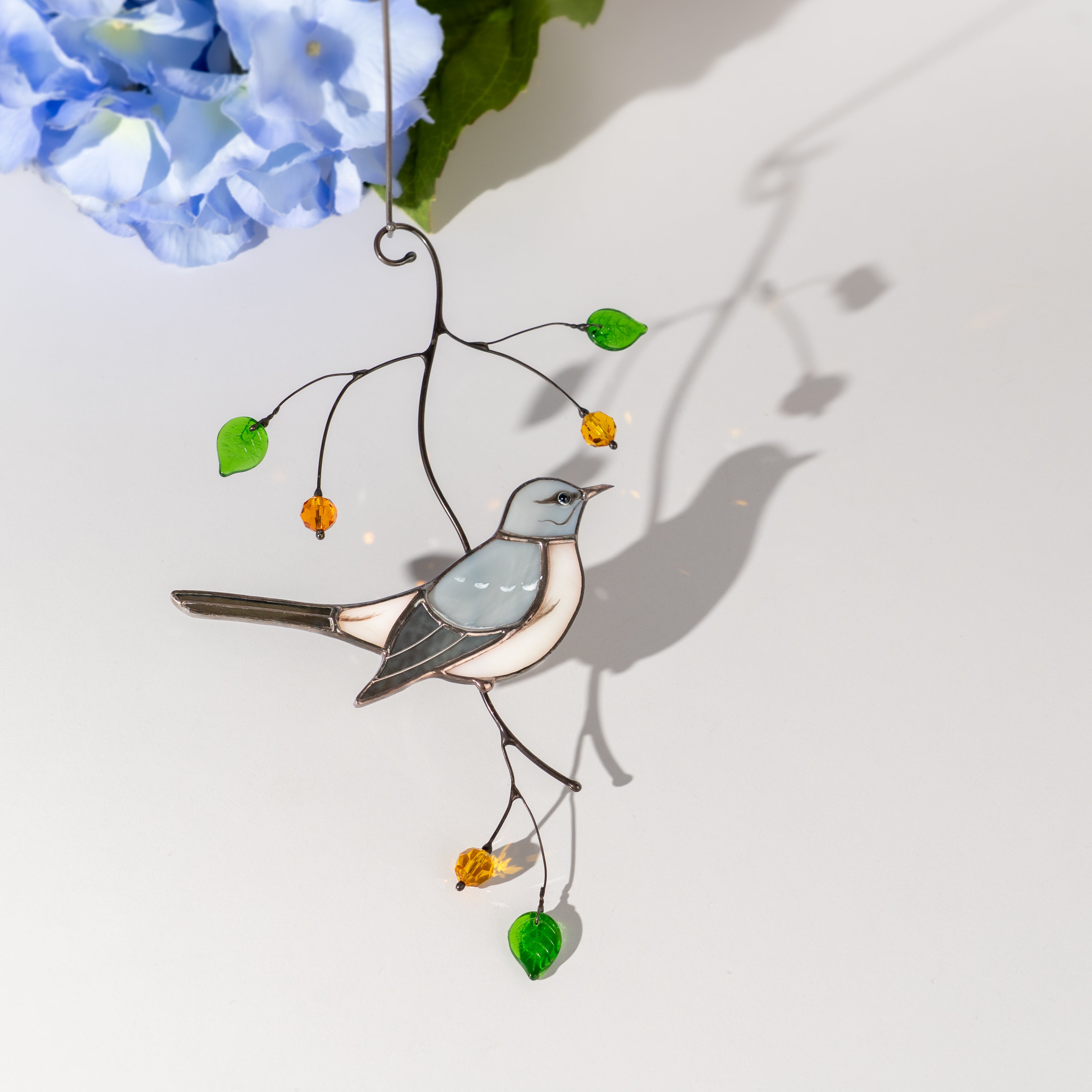 Mockingbird suncatcher with shadow play and soft flowers nearby.