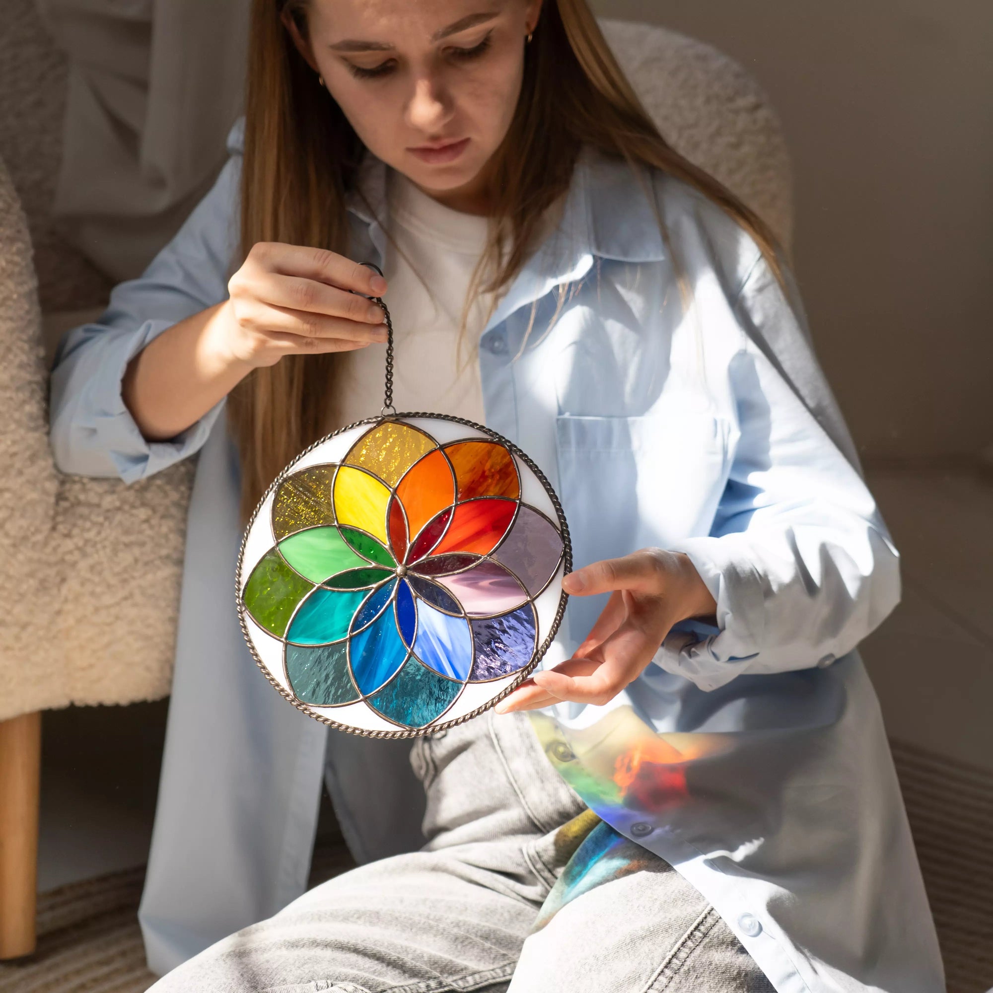 Woman holding rainbow stained glass mandala with bright reflections indoors
