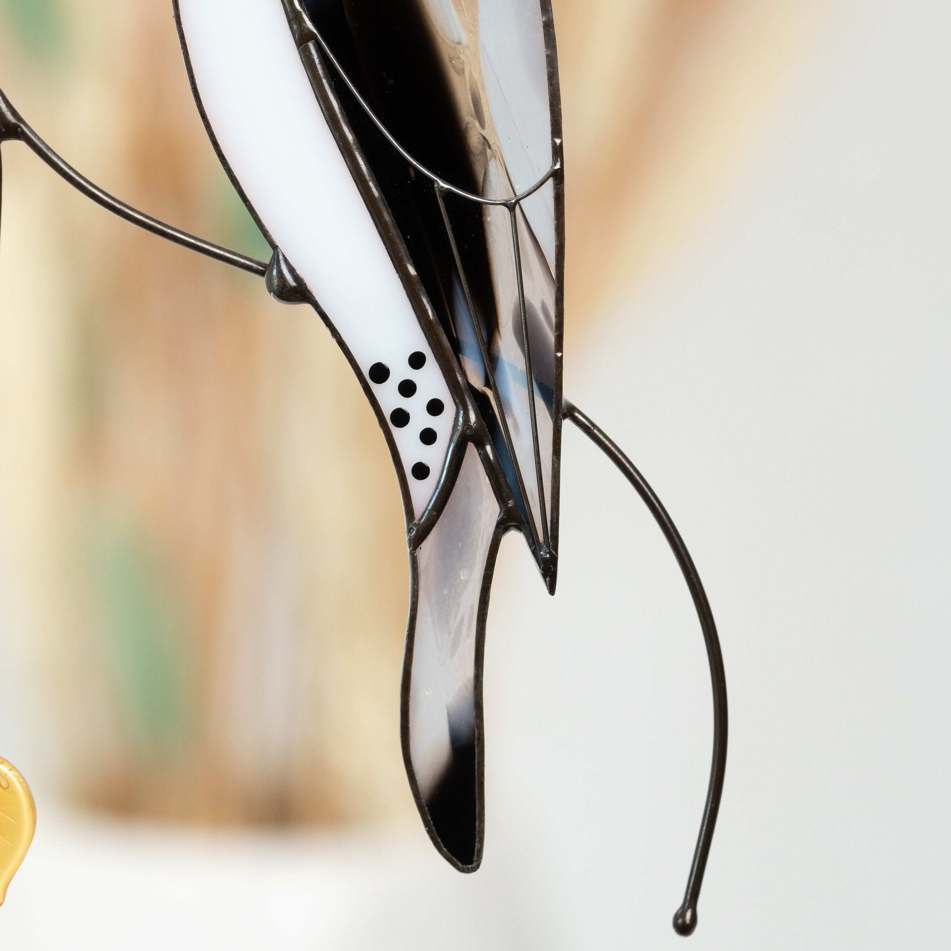 Bottom part of stained glass woodpecker showing black tail and dotted white belly, detailed curved wirework