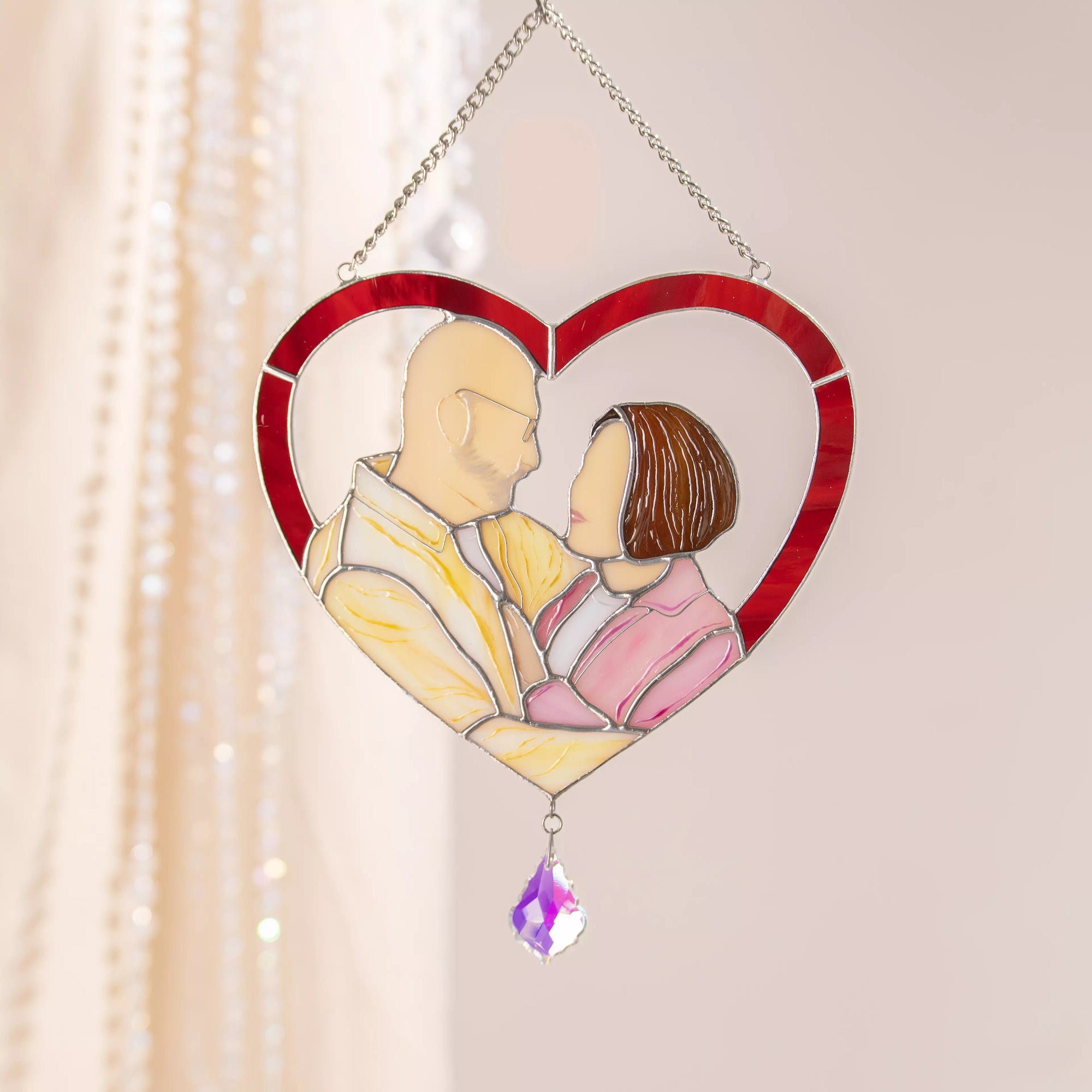 Heart-shaped custom stained glass panel with a couple and a teardrop pendant on a light background