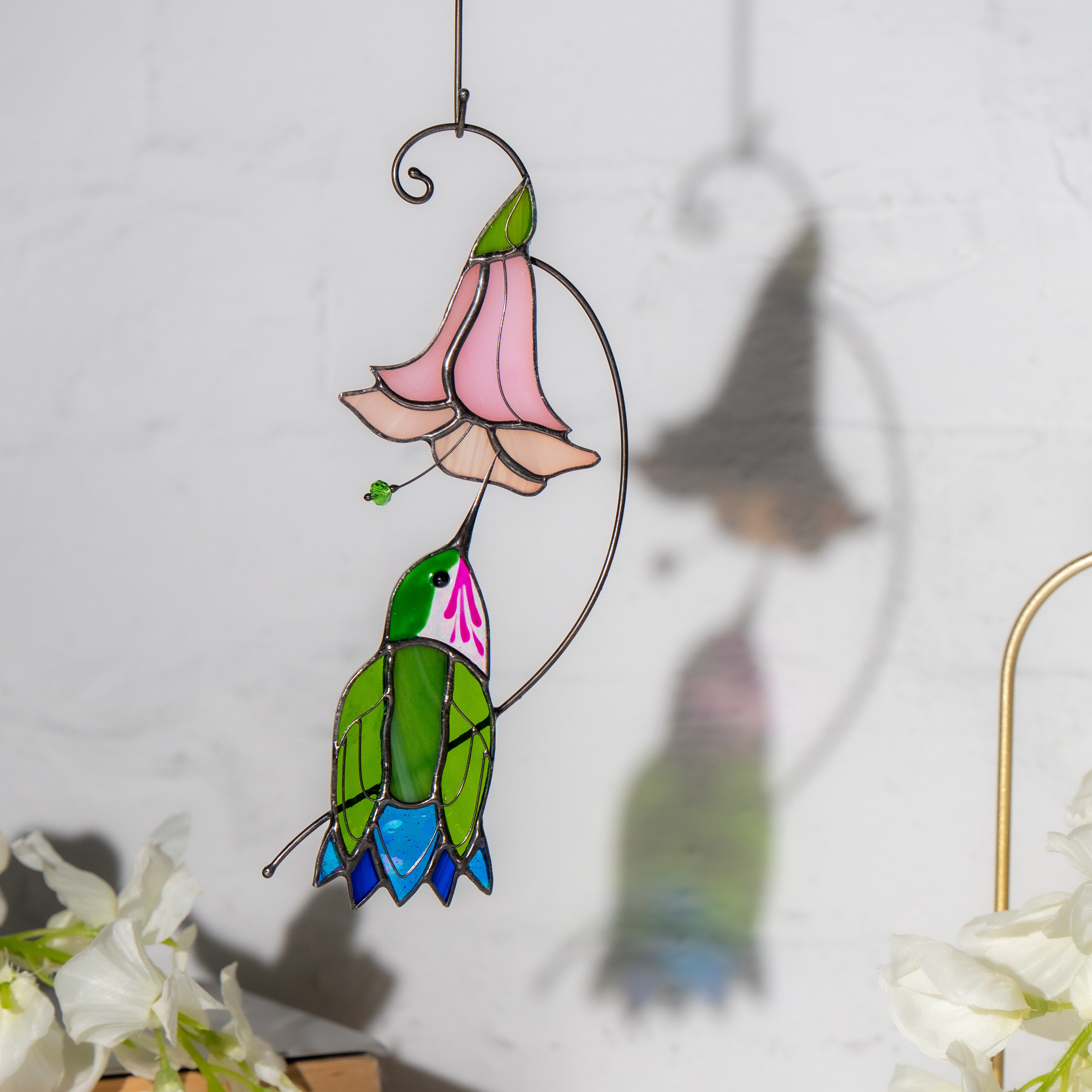 Photo of the stained glass hummingbird and flower against a white wall, casting a colorful shadow on the background.