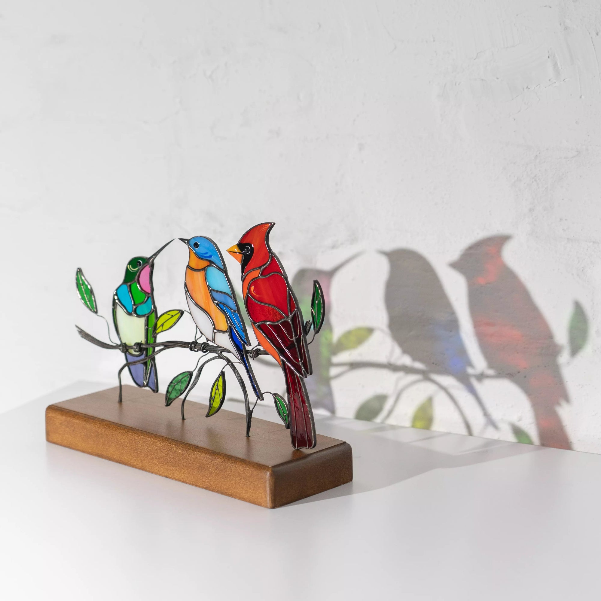 Stained glass bird trio on base casting colorful shadows on white wall