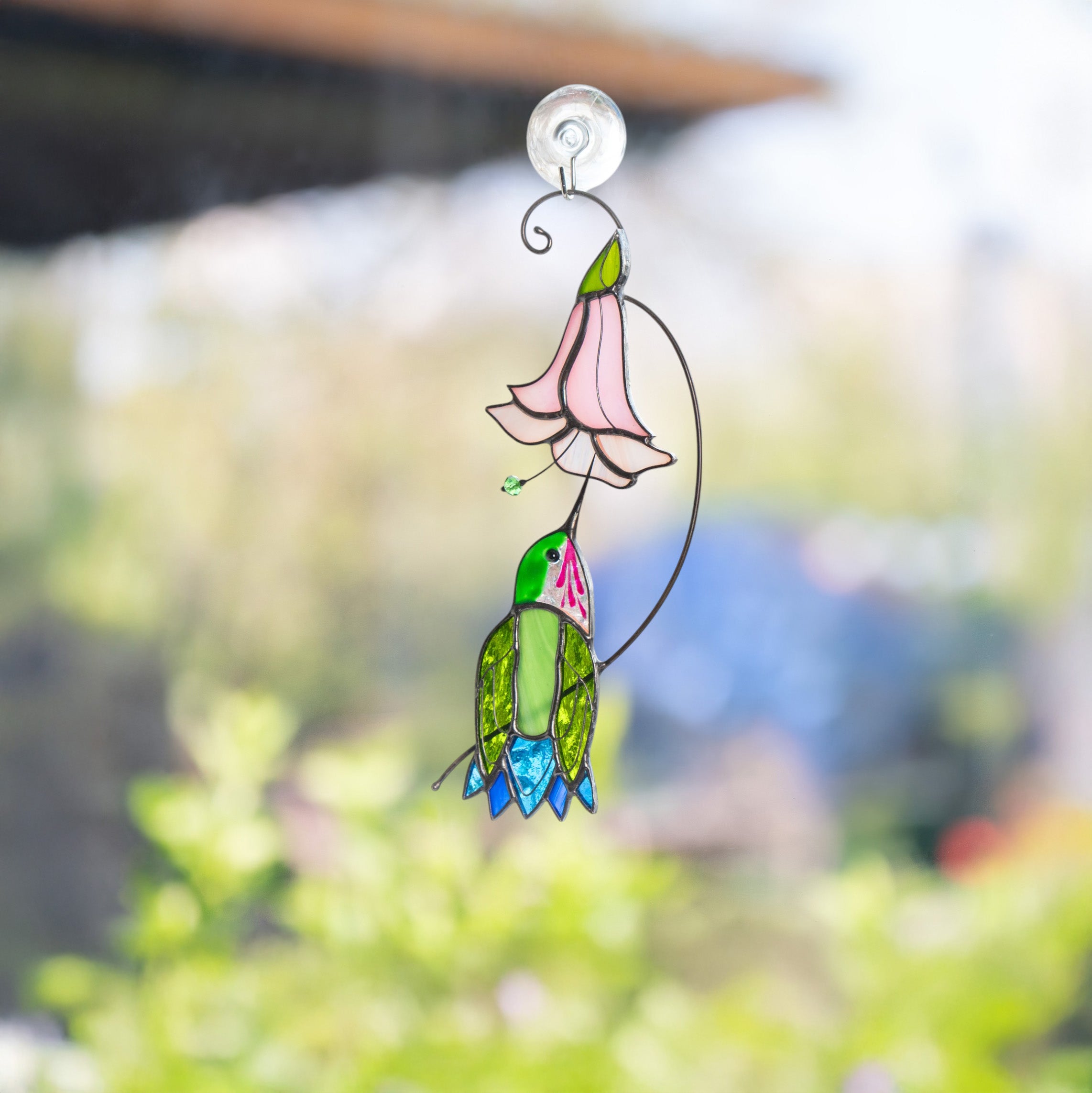 Image of the stained glass suncatcher attached to an outdoor window with bright garden in the background.
