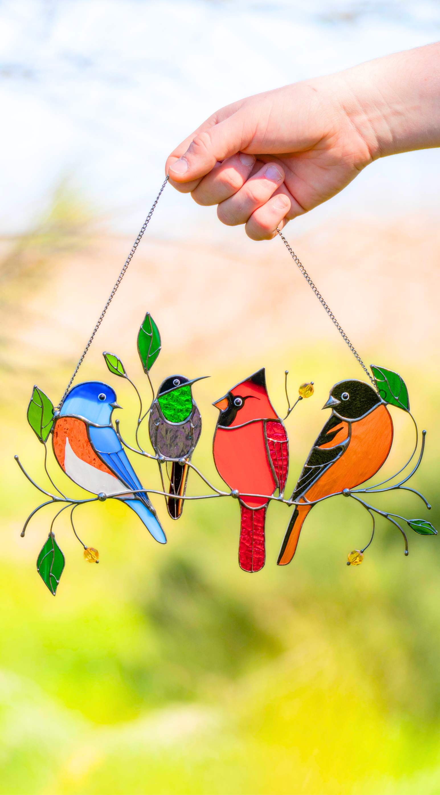 A hand holding stained glass decor featuring birds