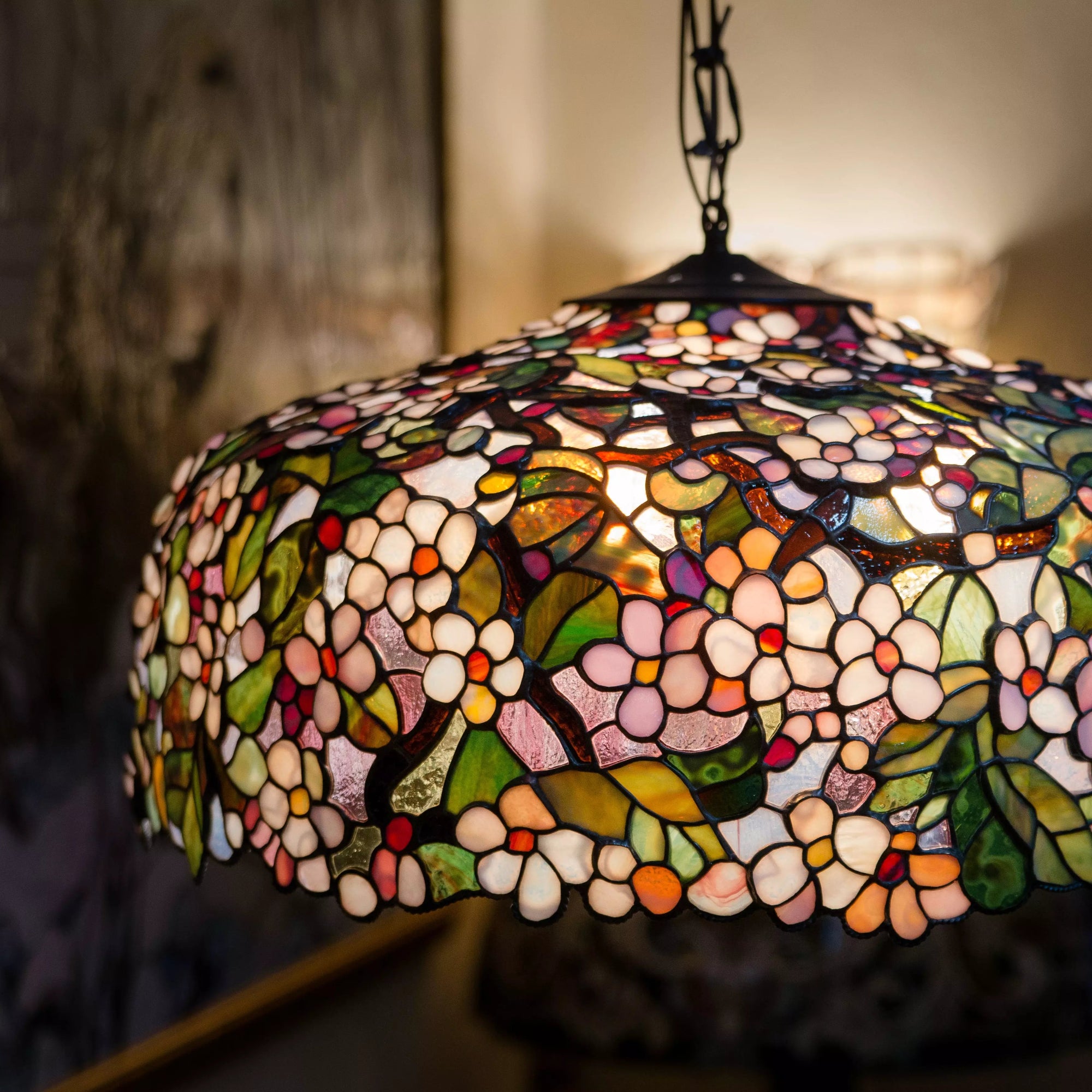 Hanging stained glass chandelier lit from inside, displaying a floral pattern with warm pink and green tones.