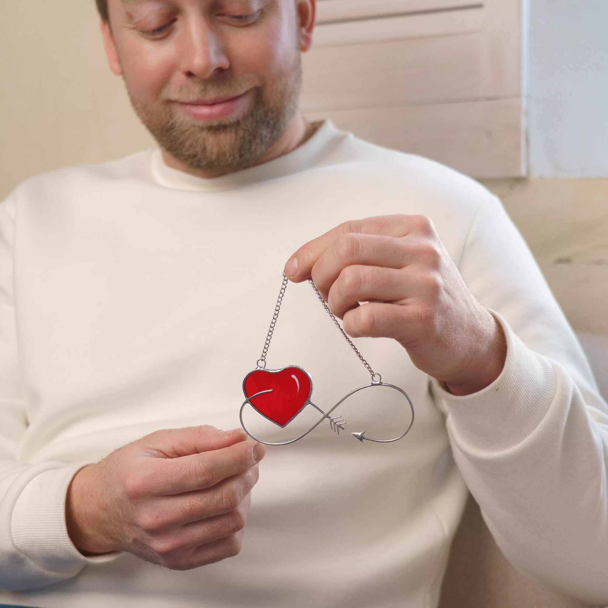 Man holding an infinity stained glass heart suncatcher featuring a red glass heart and arrow.