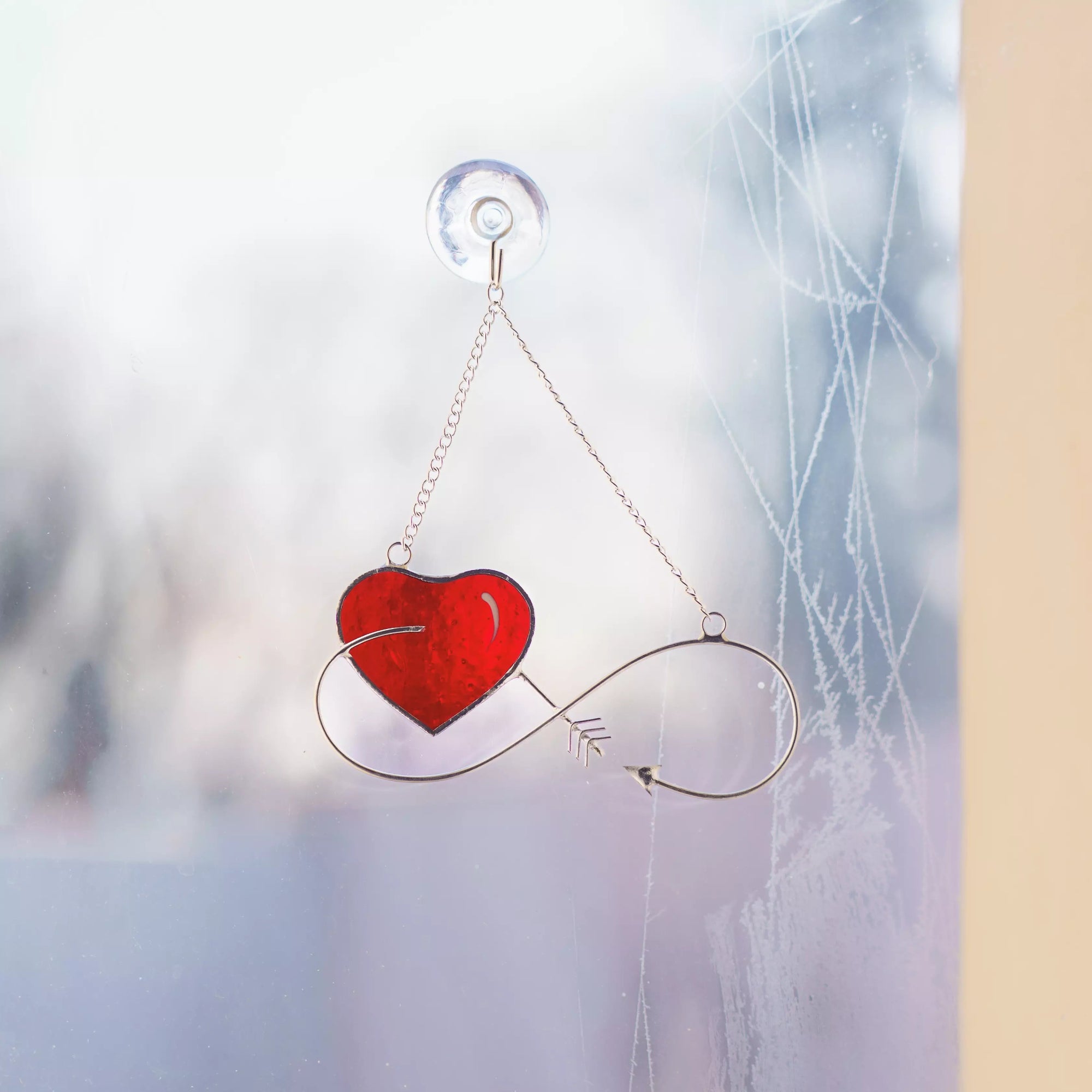 Infinity stained glass heart suncatcher hanging on a window using a suction cup.