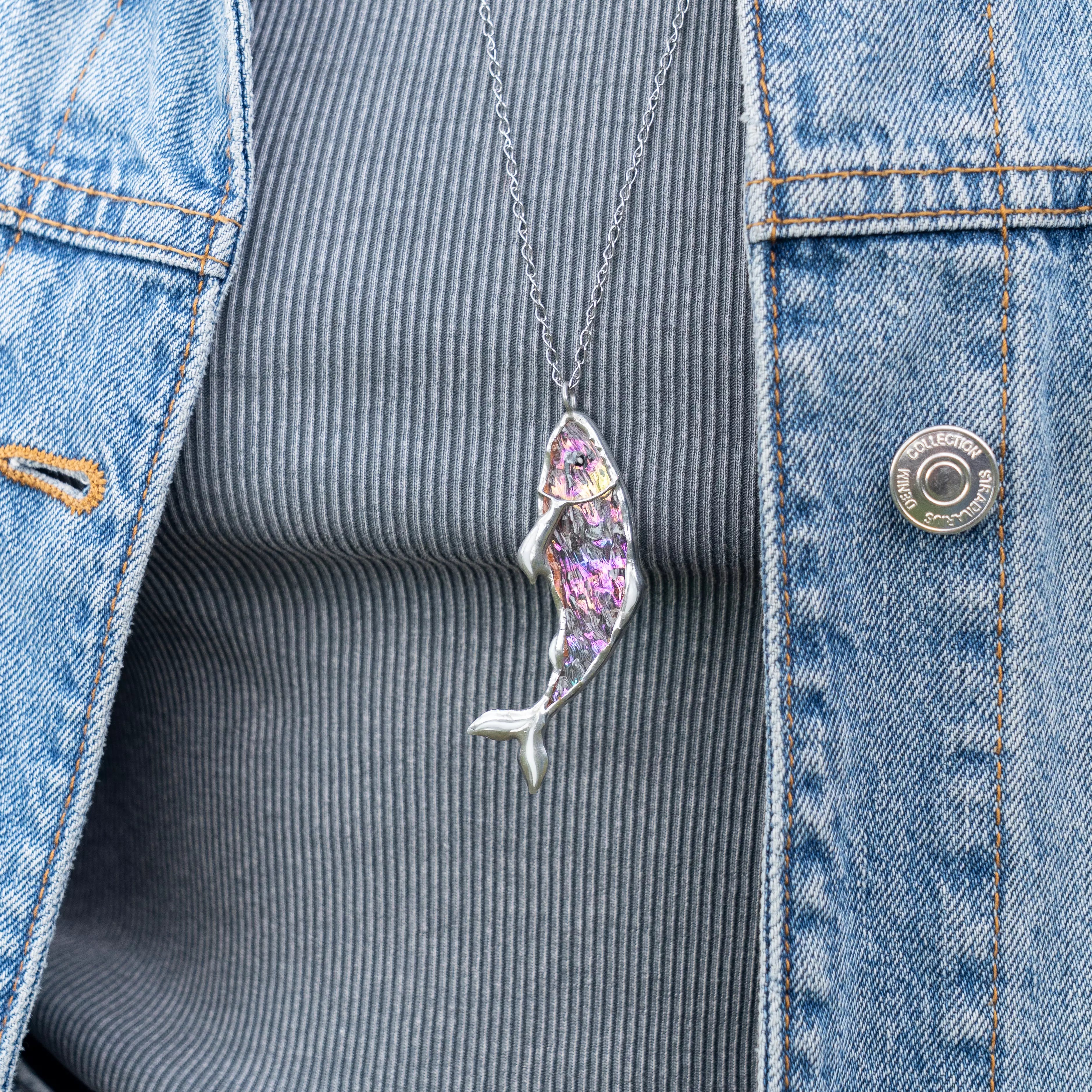 Woman wearing iridescent stained glass fish necklace over grey ribbed top and denim jacket
