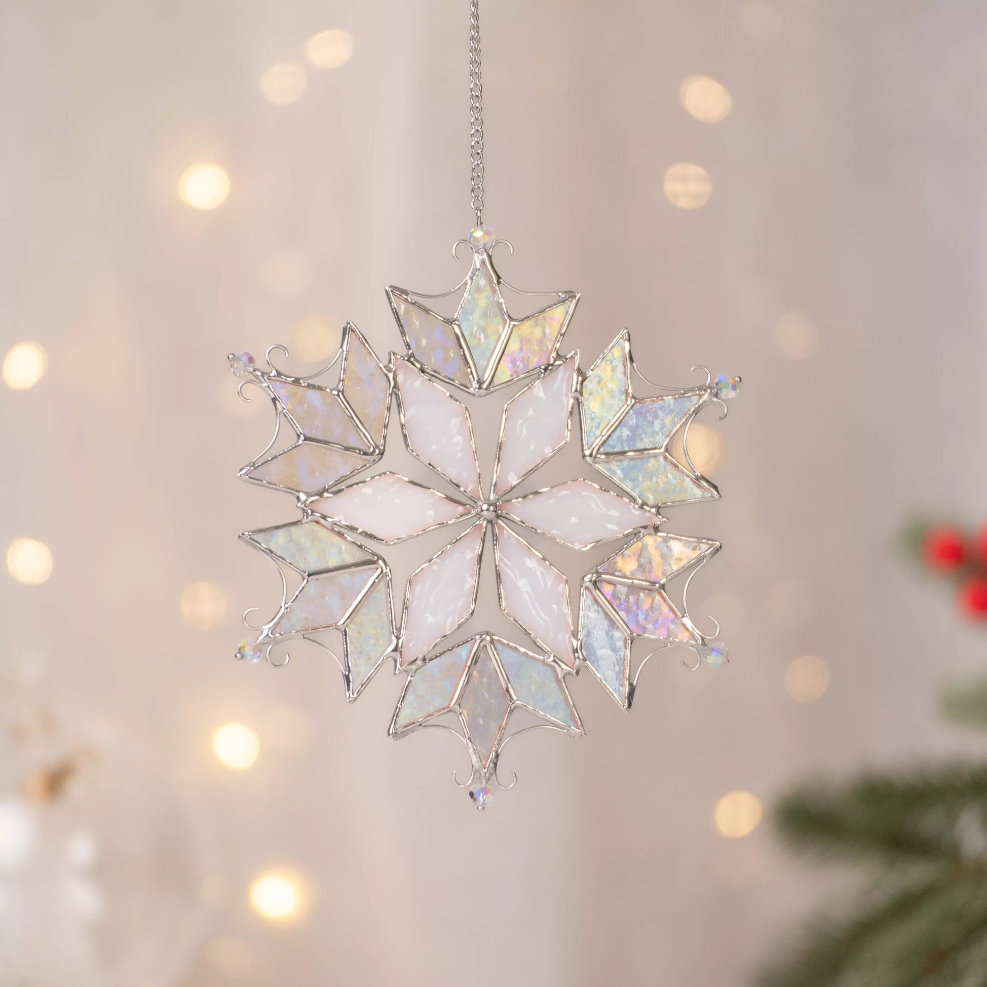 Stained glass snowflake ornament with opal and iridescent glass pieces hanging against warm blurred holiday lights.
