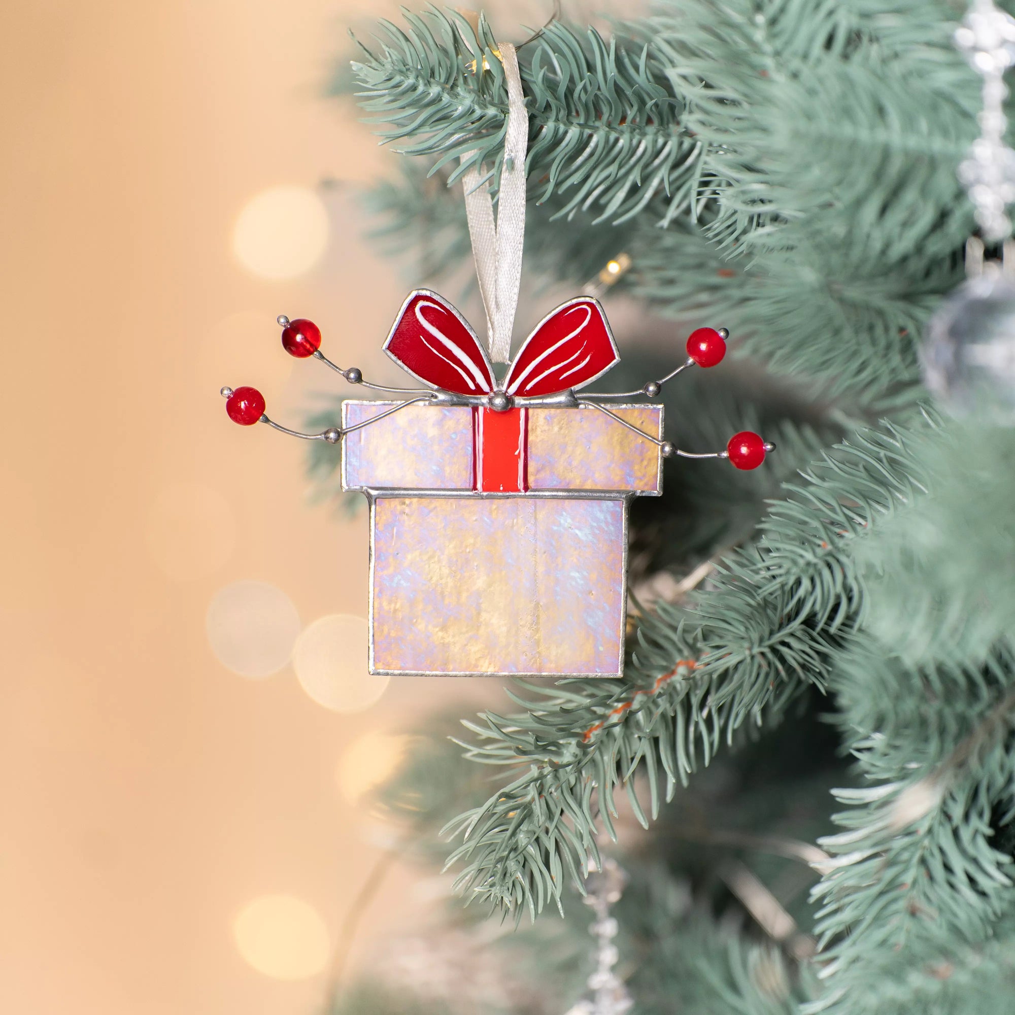 Iridescent stained glass gift box ornament with red bow and beads, hanging with a white ribbon.
