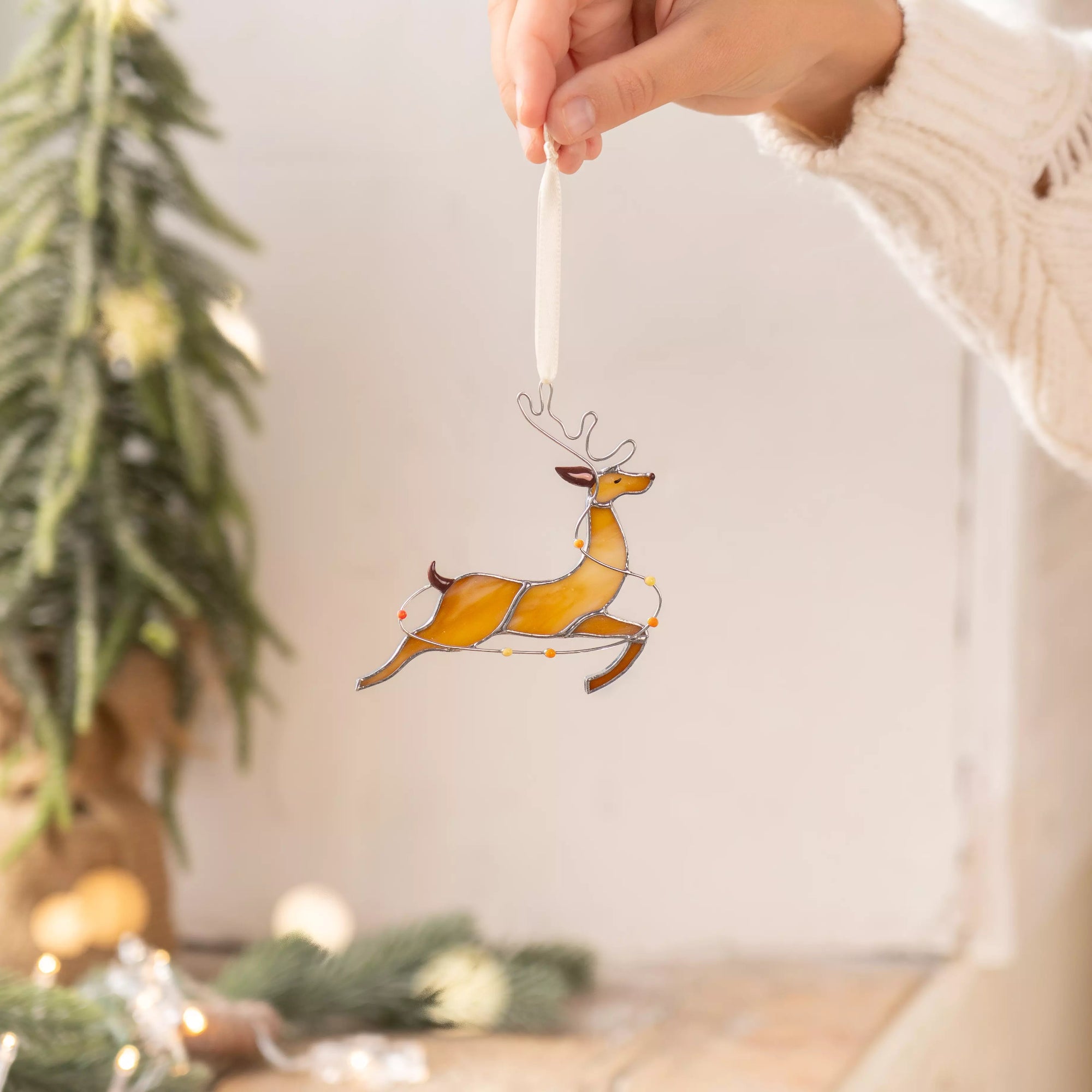 Hand holding stained glass reindeer jumping with colorful lights wrapped around its body