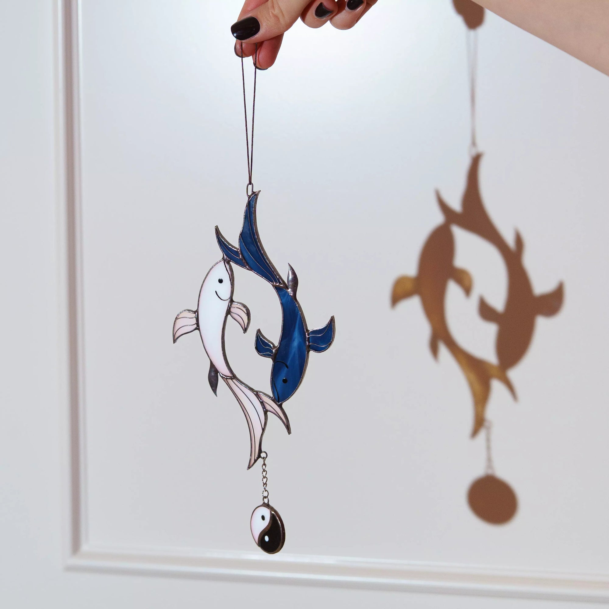 A hand holding a koi fish stained glass suncatcher that casts a beautiful blue shadow on the wall.