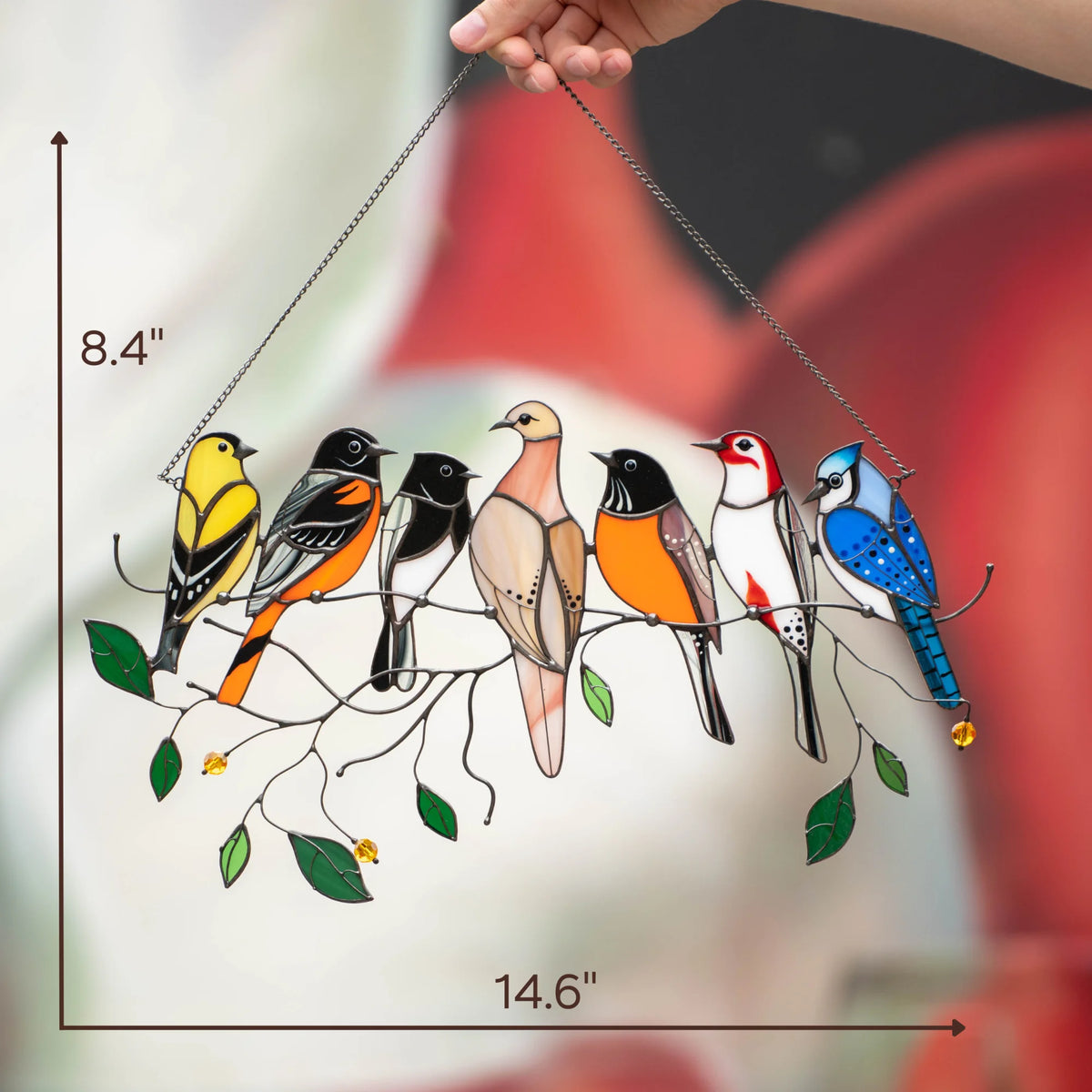 Hand holding a stained glass bird suncatcher with size indicators showing 14.6 inches wide and 8.4 inches tall, colorful birds on a leafy branch.